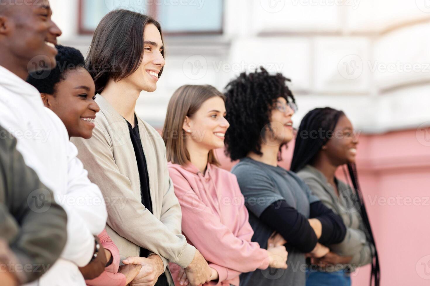 Multiracial millennial people holding crossed hands, making strike on the street, side view, panorama. Positive multiethnic men and women students activists standing in a row, making live shield photo