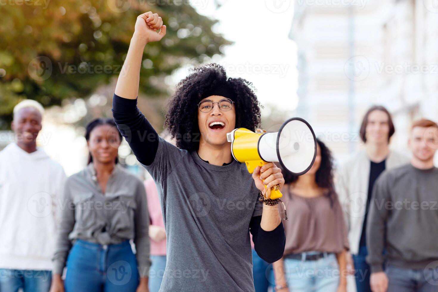 Enthusiastic mixed race millennial man with loudspeaker leading strike against lockdown rules on the street, standing over multiracial group of demonstrators, chanting slogans, panorama photo