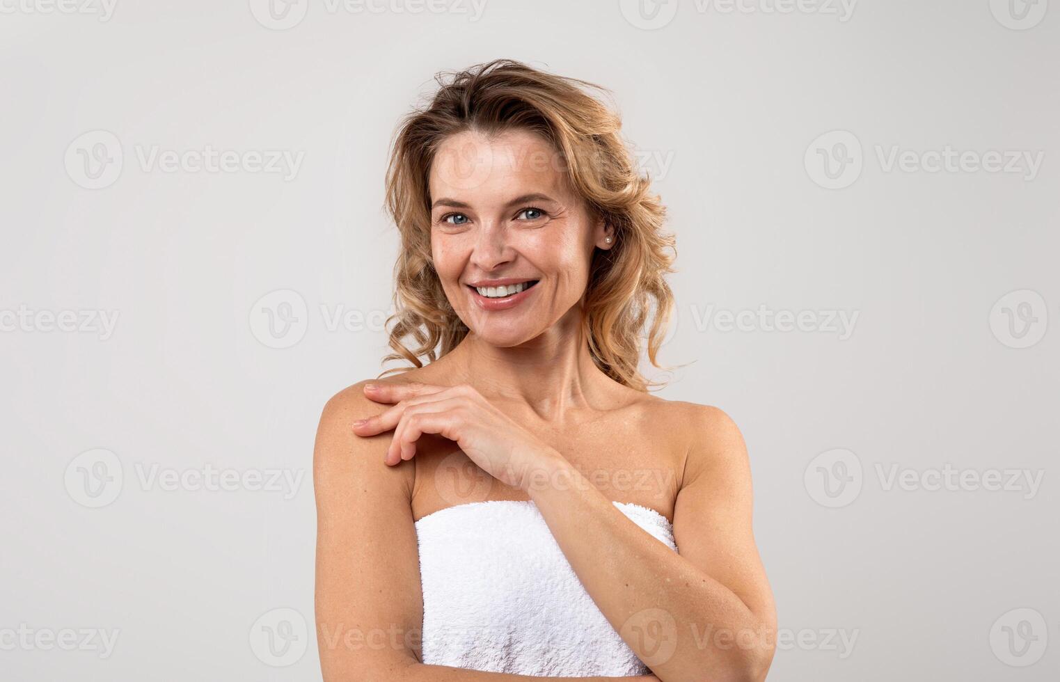 Portrait Of Pretty Middle Aged Female Wrapped In Bath Towel Posing Over Light Grey Background, Attractive Woman With Beautiful Skin Smiling At Camera, Enjoying Self-Care Treatments, Copy Space photo