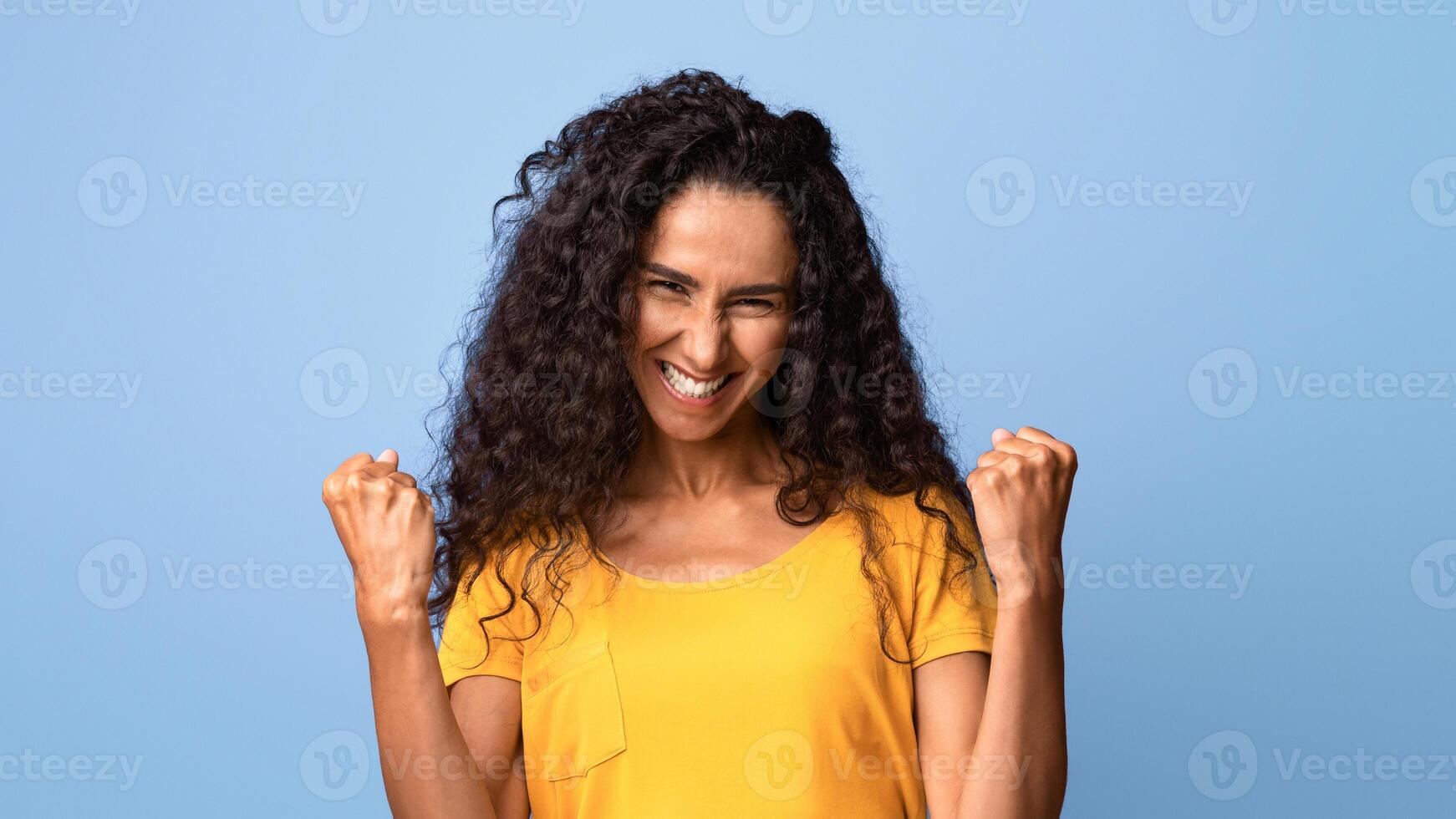 Joy Of Success. Euphoric Young Brunette Woman Celebrating Victory With Clenched Fists Over Purple Studio Background, Raising Hands, Excited Lady Cheering Luck, Portrait Of Happy Winner, Copy Space photo