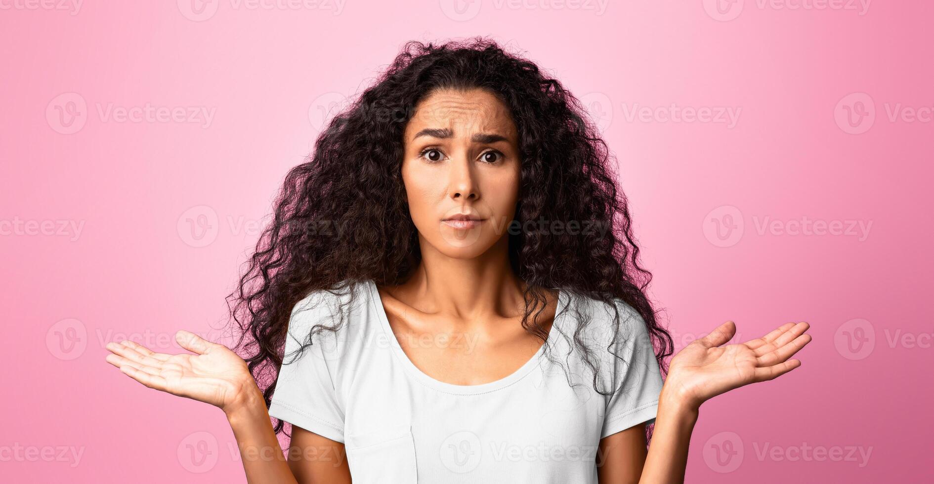 I Don't Know. Concerned young woman shrugging shoulders with spreaded hands, unsure brunette lady looking at camera with misunderstanding, standing over purple studio background, copy space photo