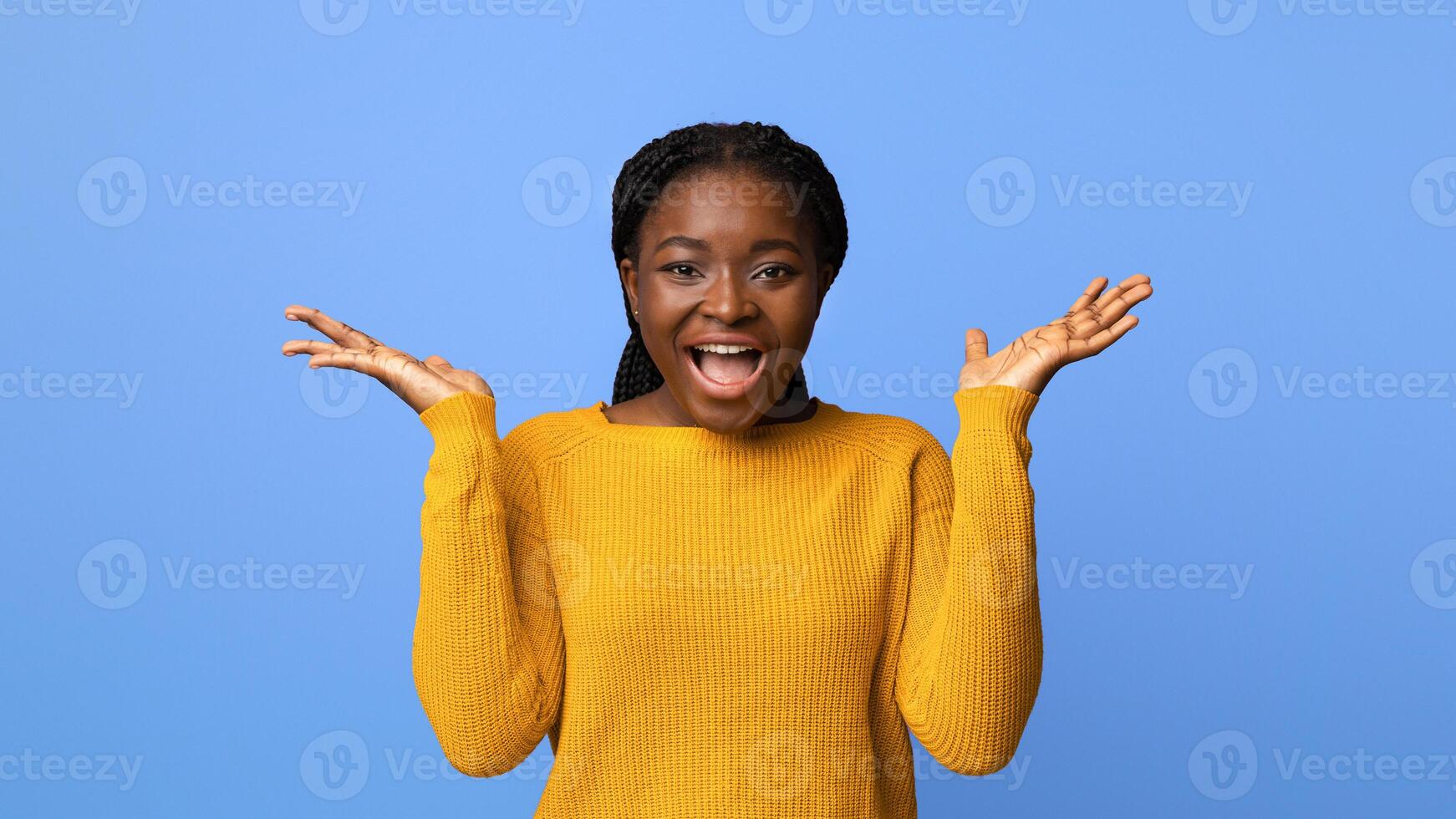 Happy Emotion. Joyful African American Woman In Yellow Sweater Exclaiming At Camera With Excitement, Raising Hands, Amazed And Surprised By Something, Posing Over Purple Studio Background, Copy Space photo