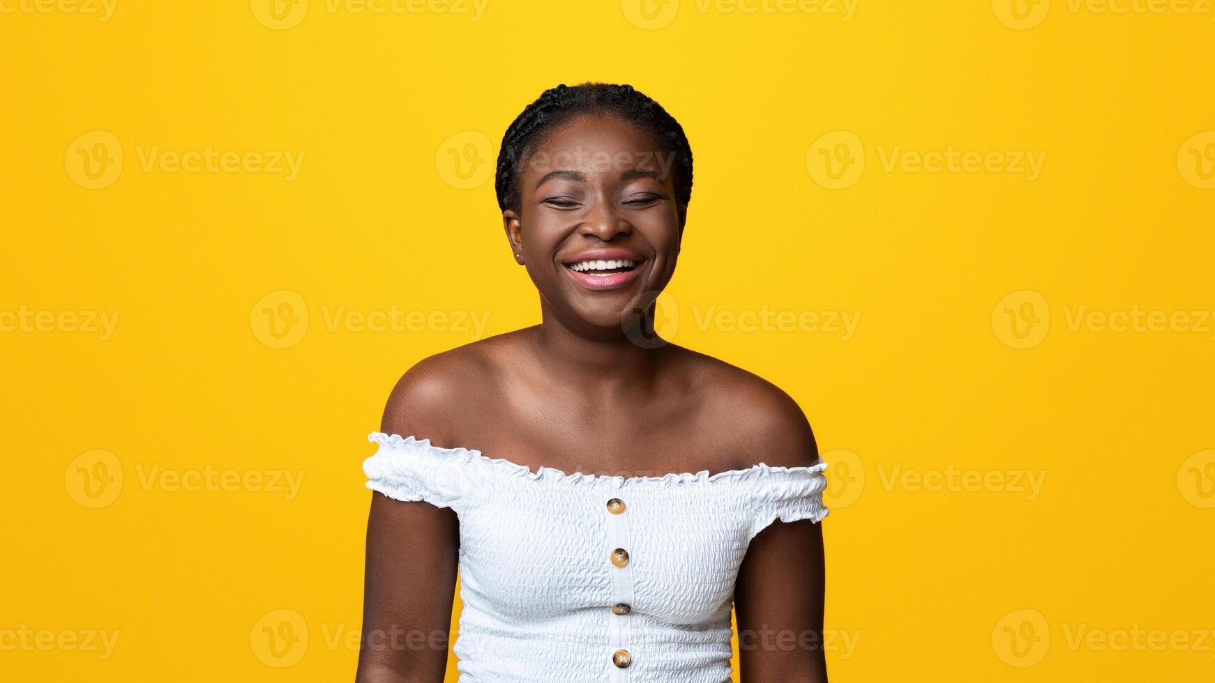 Portrait of beautiful african american lady sincerely laughing on yellow background, positive black woman having good mood, emotionally reacting to joke, joyful female smiling with closed eyes photo