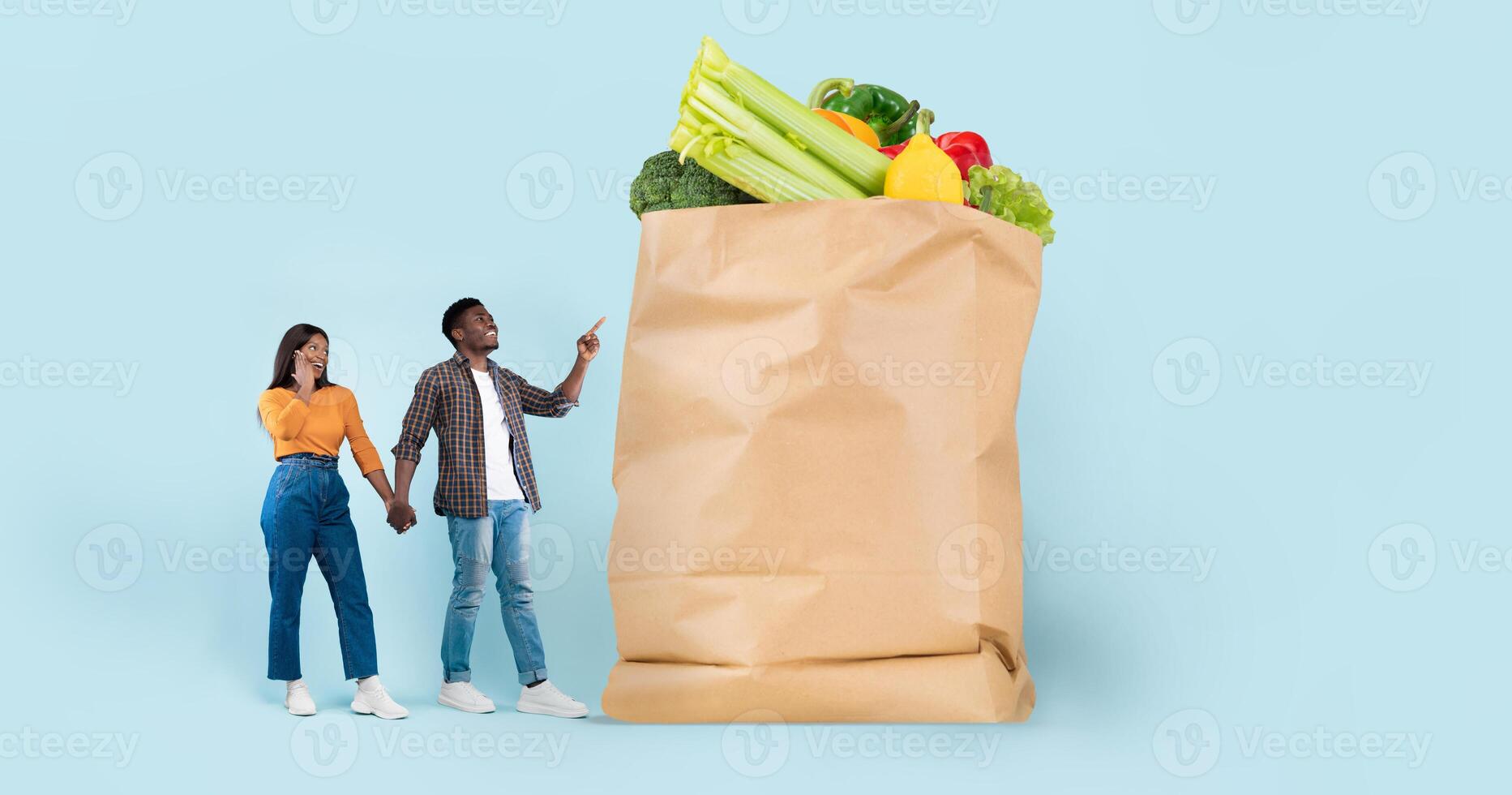 A couple stands next to a large paper bag filled with fresh vegetables. They appear cheerful, engaged in conversation about their recent grocery shopping experience. photo