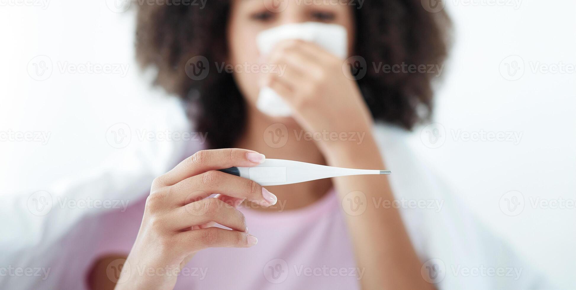 First symptoms of illness, fever, flu, colds and covid virus. Sad blurred millennial african american woman in blanket wipes nose with napkin and looks at thermometer, selective focus, free space photo