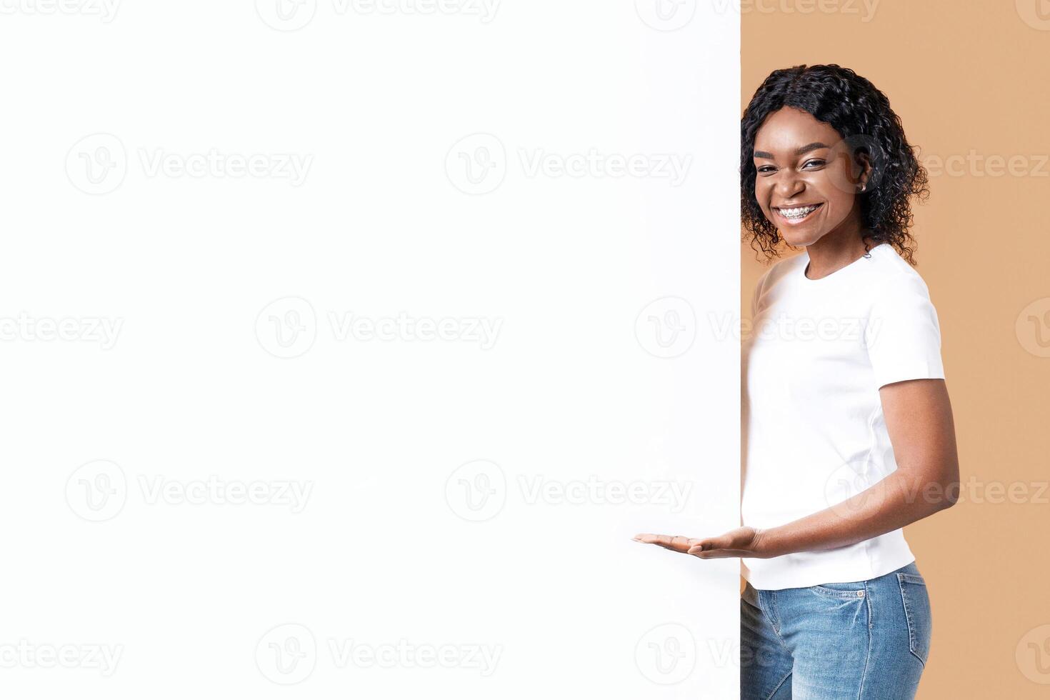 Attractive black woman showing blank advertisement board, standing on yellow studio background. Smiling african american lady posing next to big white placard for text or advertising, panorama photo
