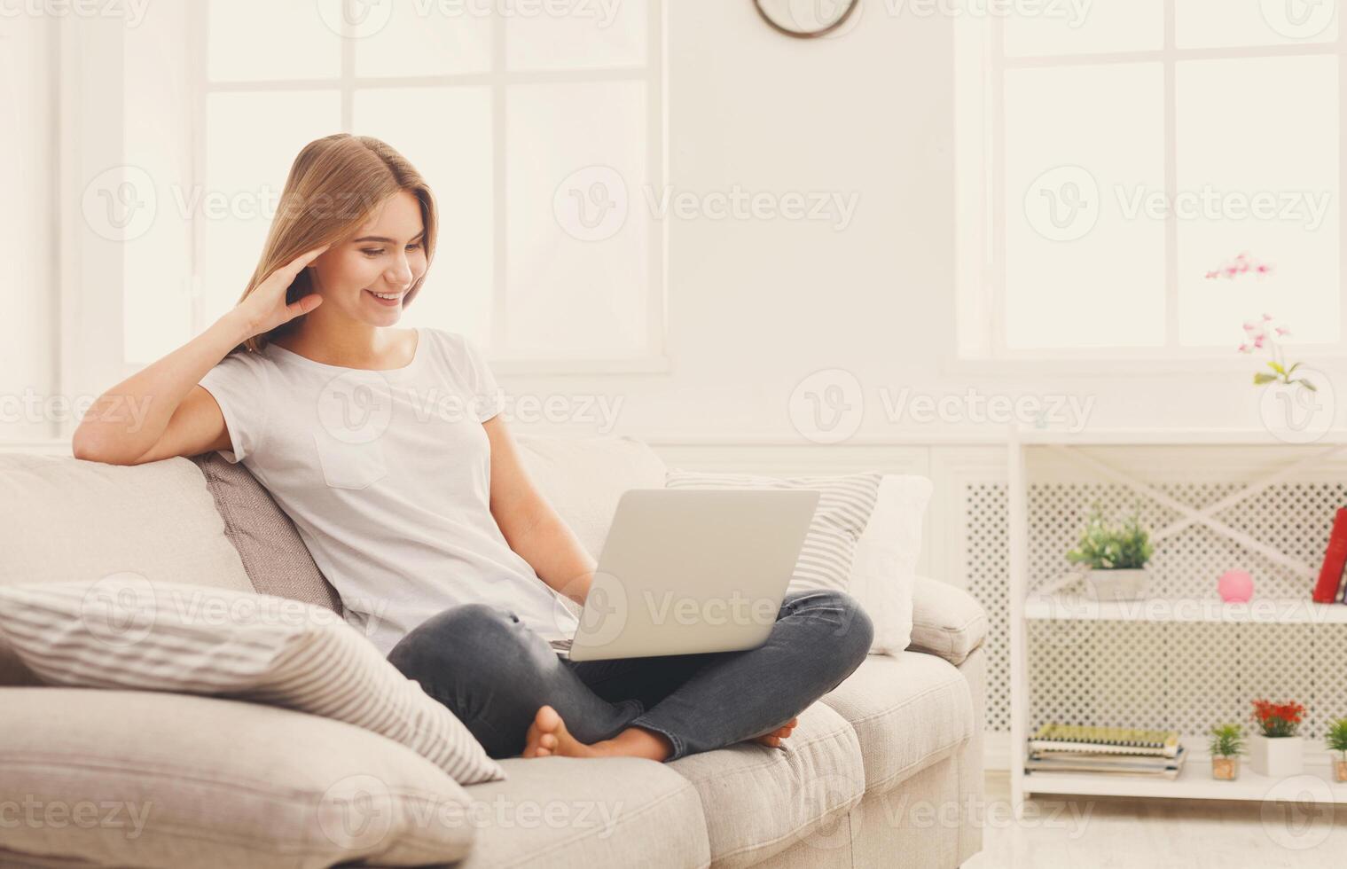 Happy girl chatting online on laptop. Smiling blonde woman messaging with friends on computer. Social media, communication and technology concept, copy space on wall photo