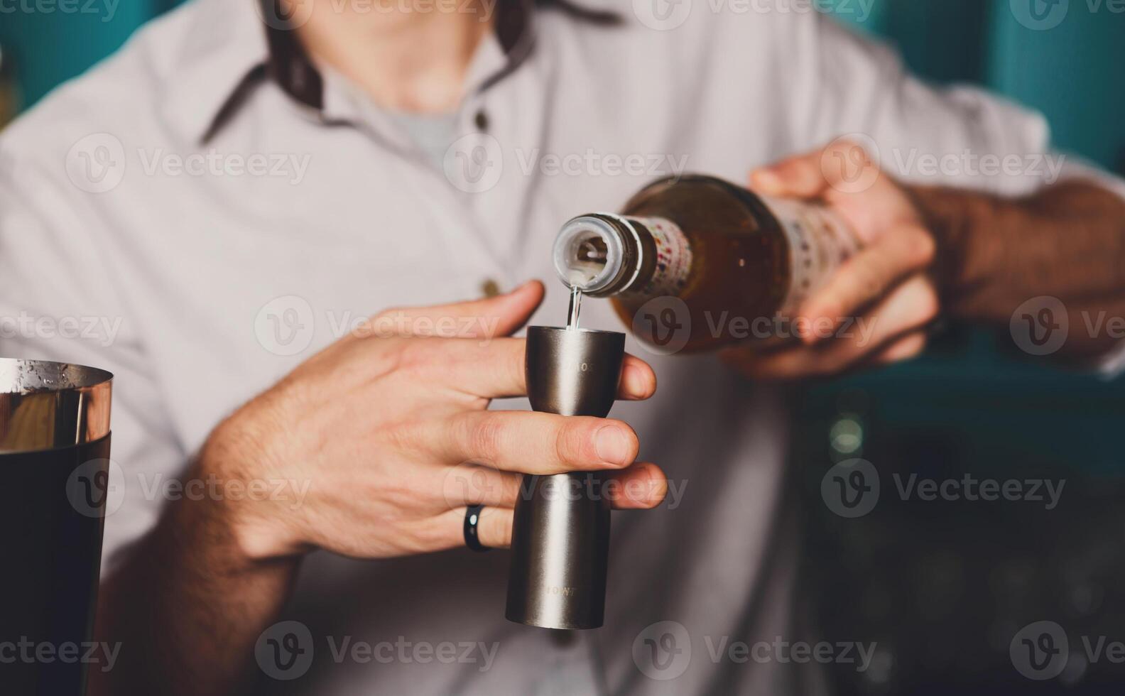 Barman's hands in bar interior making alcohol shot cocktail. Professional bartender at work in bar pouring drink into measuring glass. Party time in night club photo