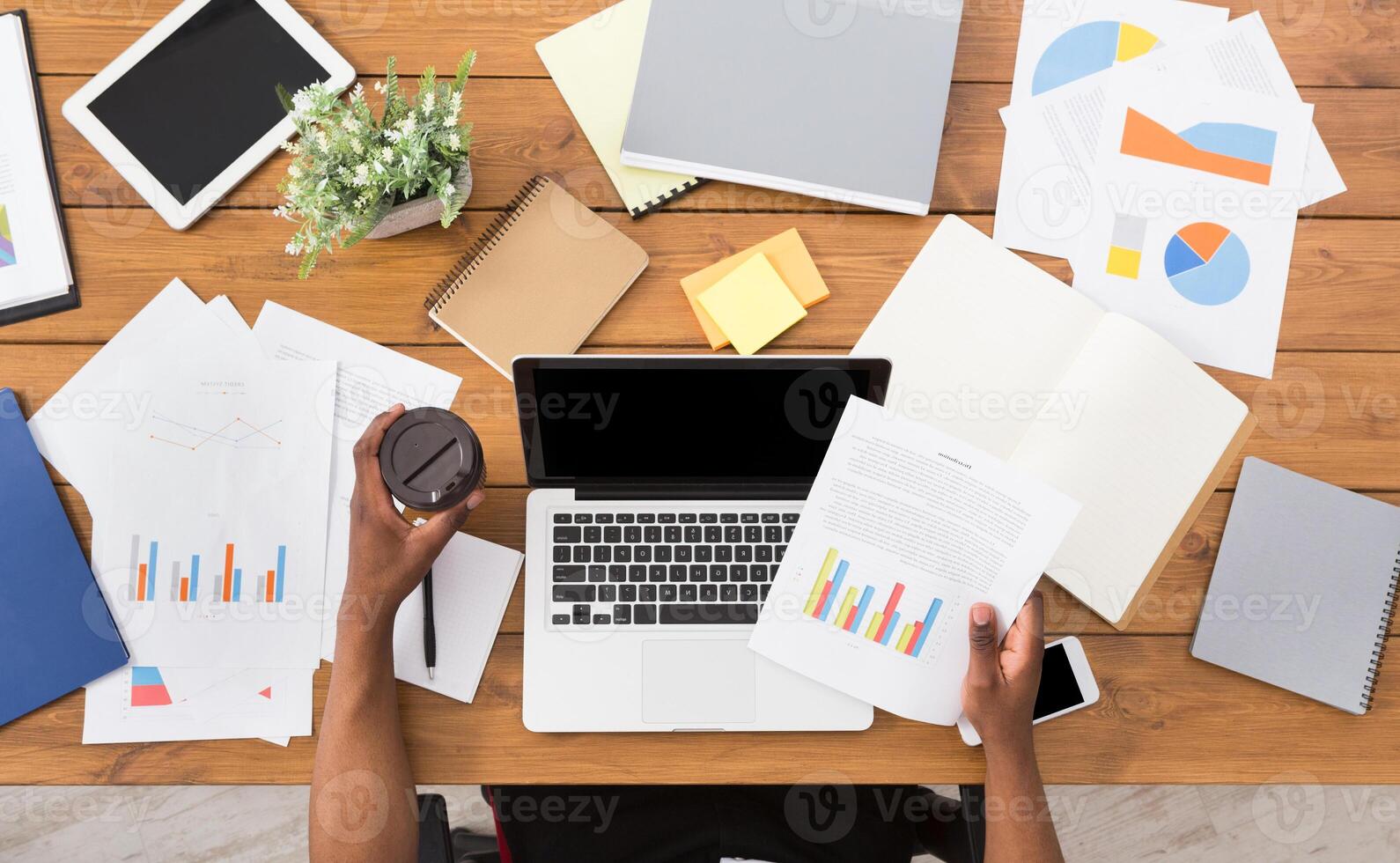 Office workspace top view. African-american businessman working at wooden desk, using laptop and various objects all around photo