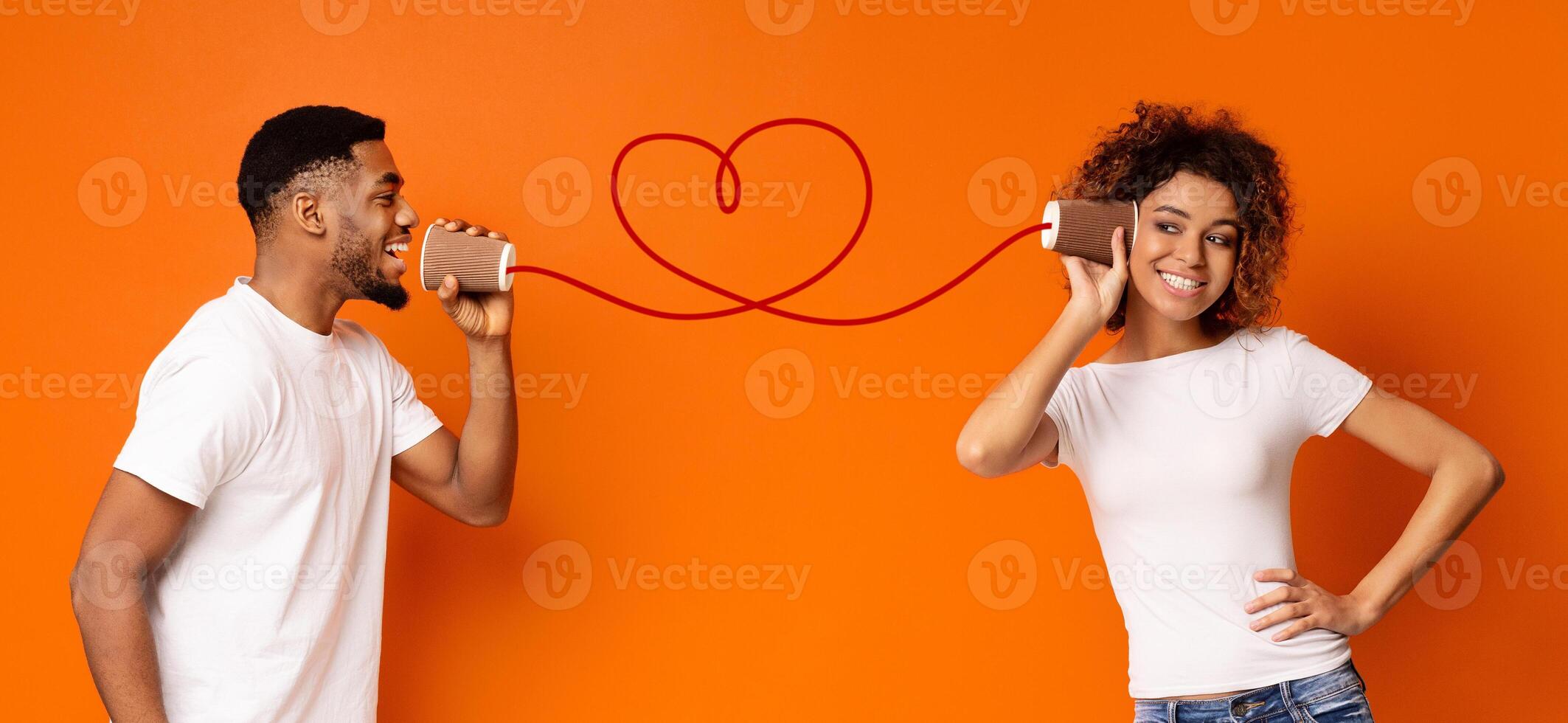 Communication and fun. Young black couple talking through tin can phone, orange background, panorama photo