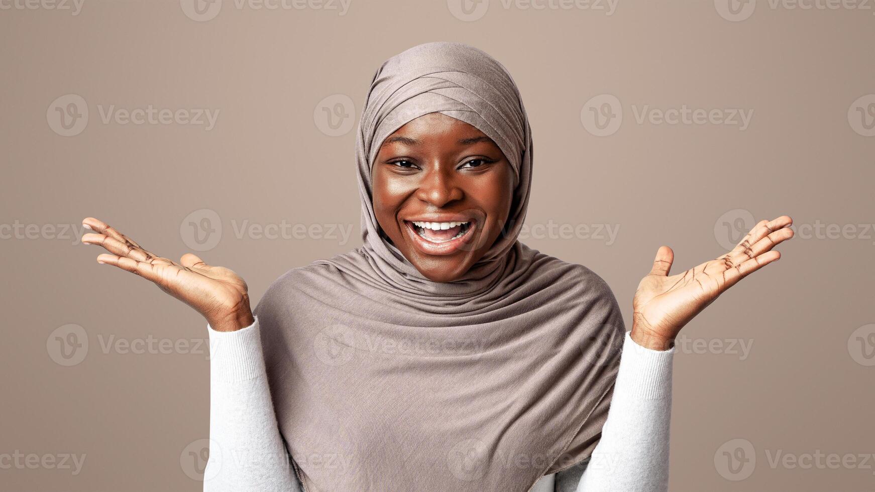 Happy black muslim lady in hijab spreading hands in excitement, exclaiming in amazement, glad to see somebody, experiencing happy shock, standing over light studio background with copy space photo