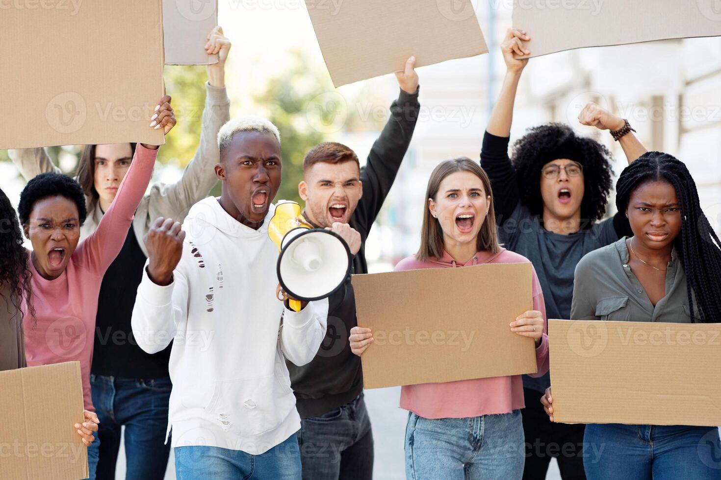Furious students leading by african american young man walking by street with empty placards and chanting slogans. Multiracial group of millennials striking against coronavirus pandemic restrictions photo