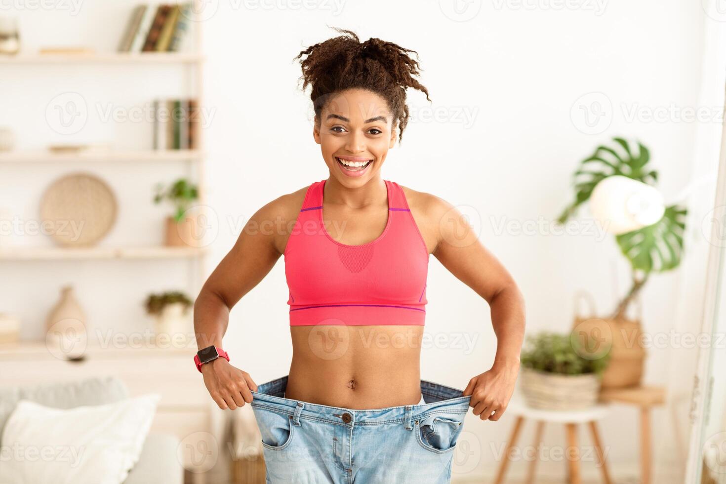 Successful Weight Loss. Happy African Woman After Slimming Showing Her Old Oversize Pants Standing Indoors, Smiling To Camera photo