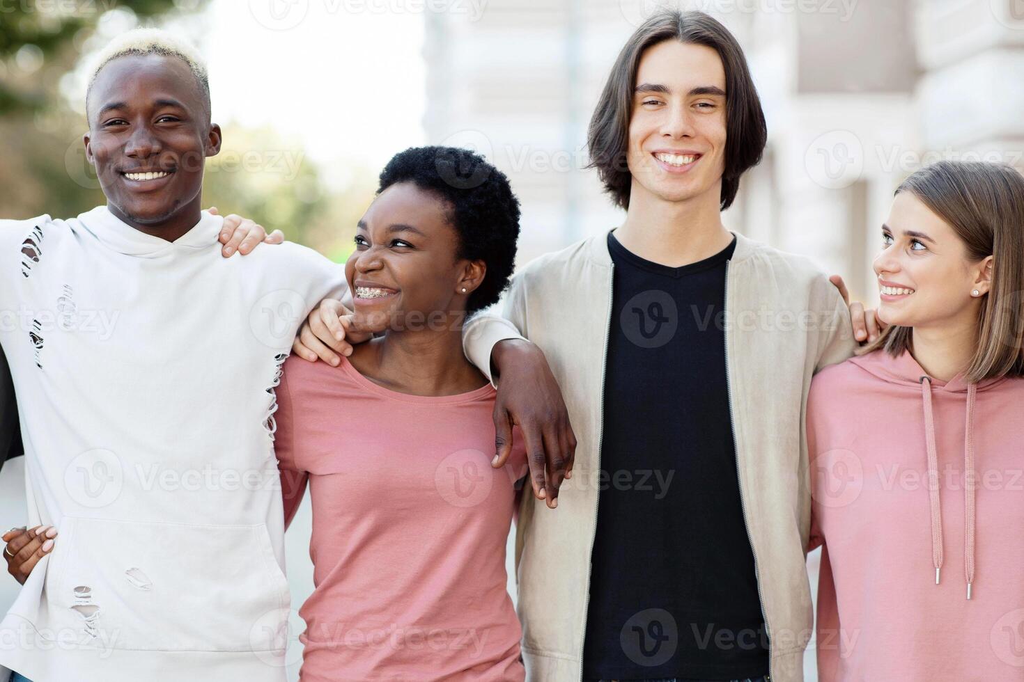 International group of friends in casual outfits smiling and hugging on the street, carefree multiracial students standing in a row and embracing outdoors, closeup, panorama photo