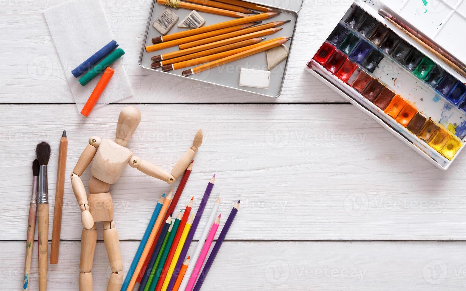 Drawing tools, stationary supplies, workplace of artist. Paints and wooden painter man with brushes on white desk, top view, flat lay, objects photo