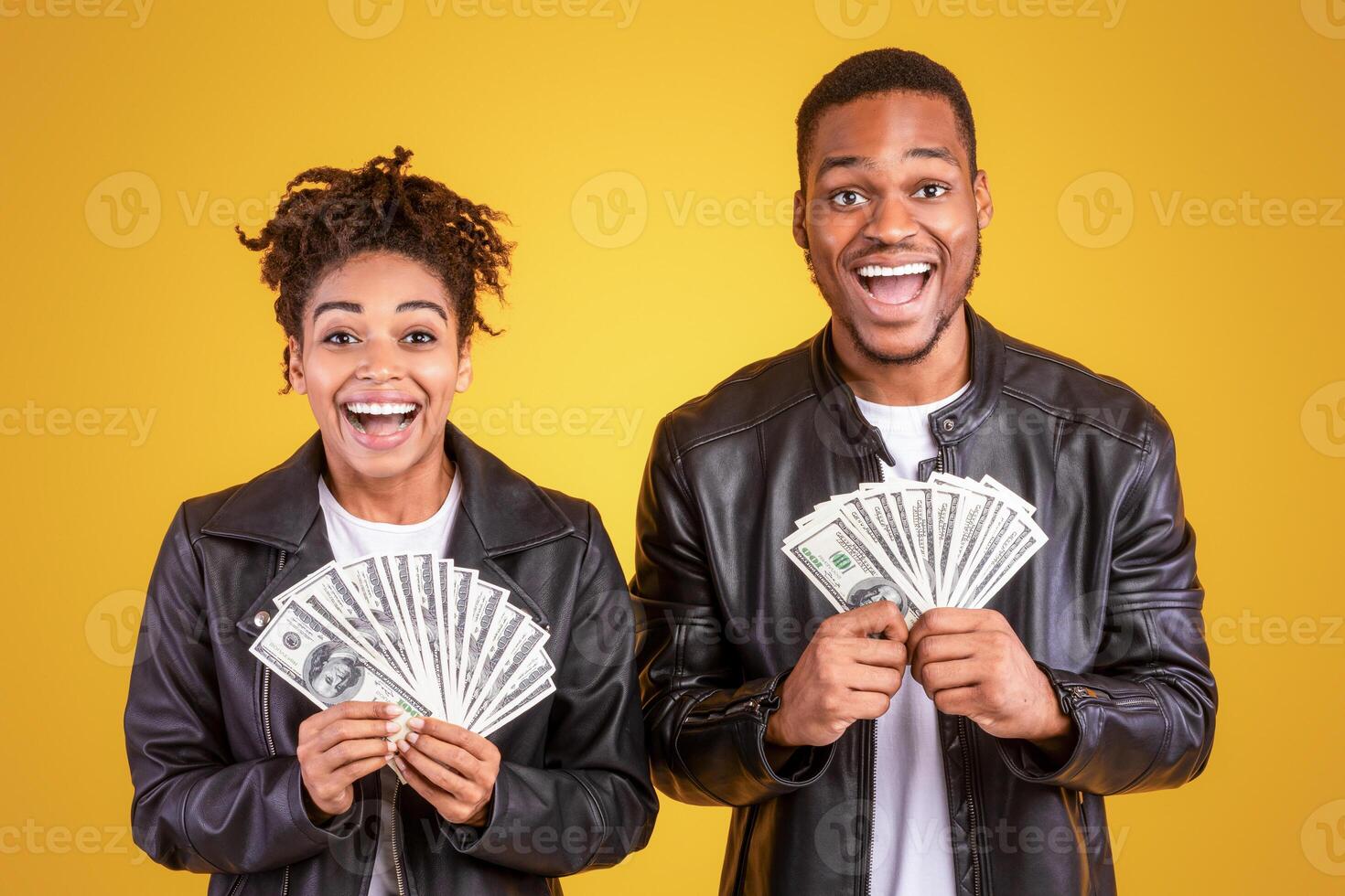 Excited Black Couple Holding Money Cash Standing Over Yellow Studio Background, Smiling To Camera. Wealth, Financial Success, Profit Advertisement Banner. Panorama photo
