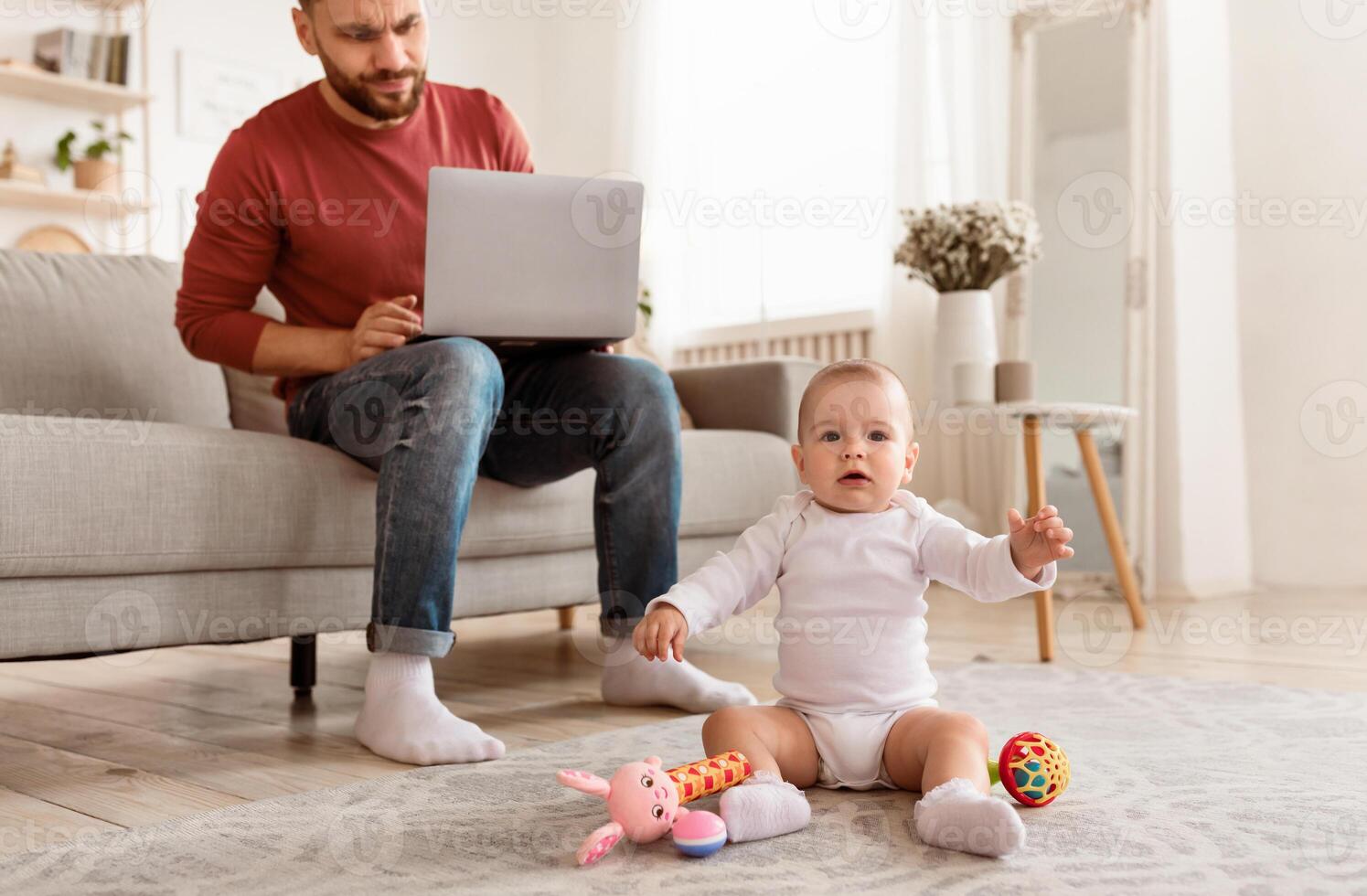 Irritated Single Father Looking At Baby Toddler While Working On Laptop Online Sitting On Sofa At Home, Selective Focus, Cropped. Paternity Leave And Parenting Problems Concept photo