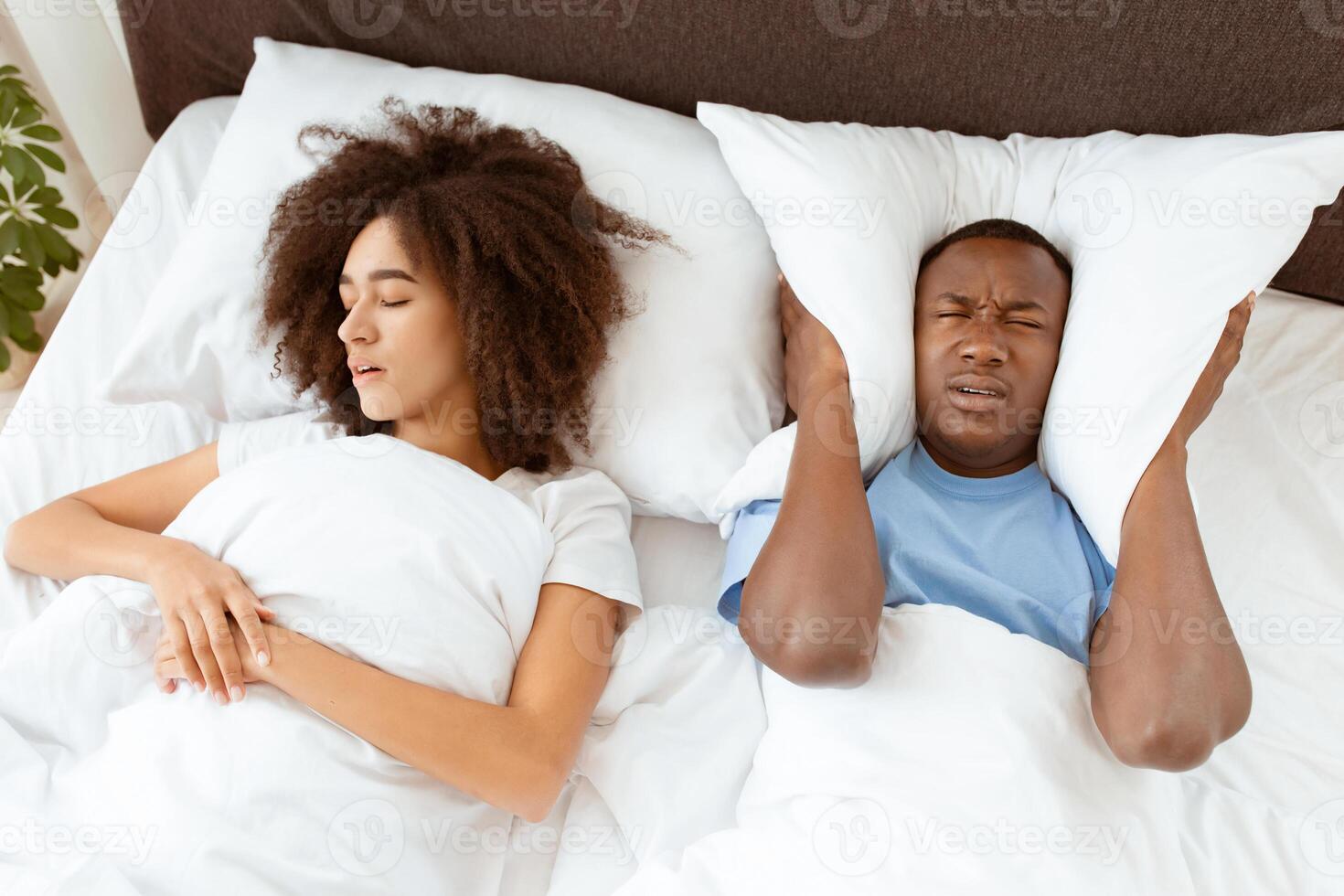 Insomnia from snoring, interfere with sleep and health problems. Millennial african american female sleeping and snoring, sad male suffers and covers his ears with pillow, empty space, top view photo