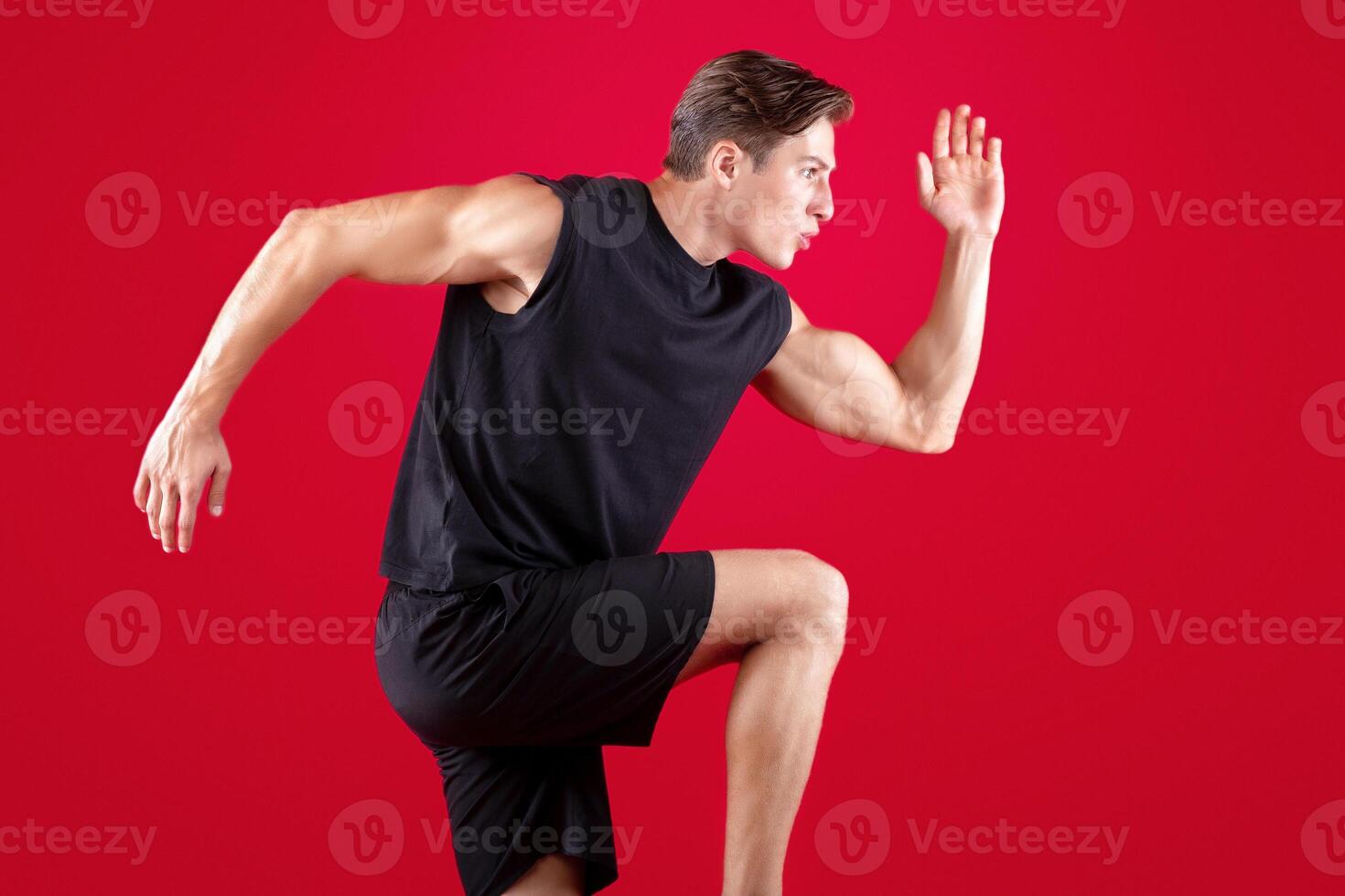 Portrait of focused young man running fast on red studio background. Side view of motivated millennial sportsman jogging, getting ready for marathon or race photo