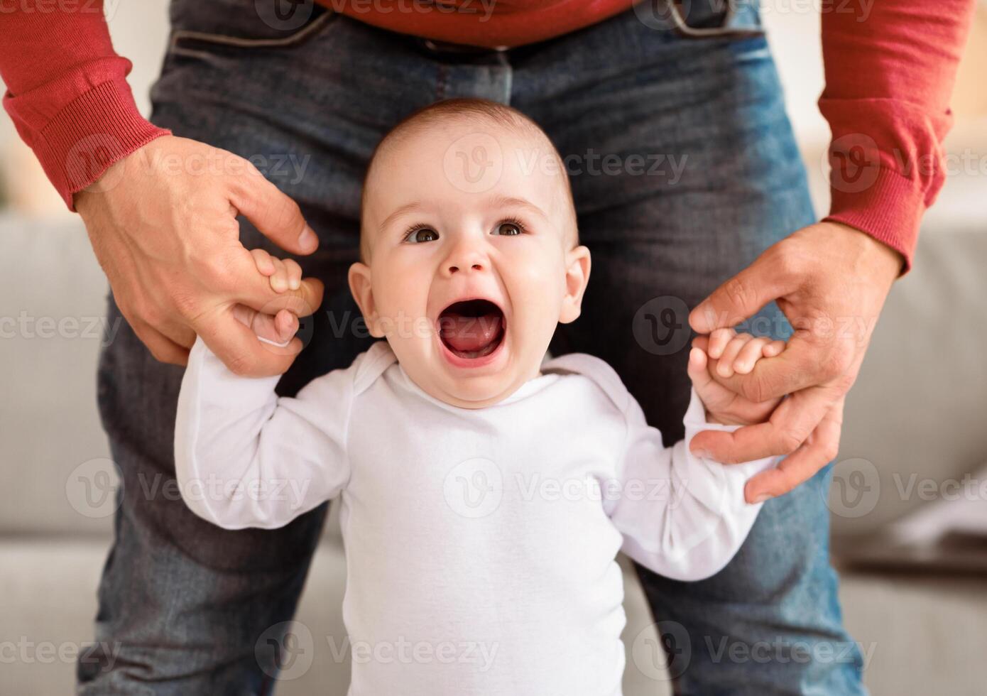 First Steps. Happy Little Baby Boy Walking Holding Father's Hands At Home. Daddy Helping His Small Son To Make First Step Indoor. Cute Family Moments And Fatherhood Concept. Cropped photo