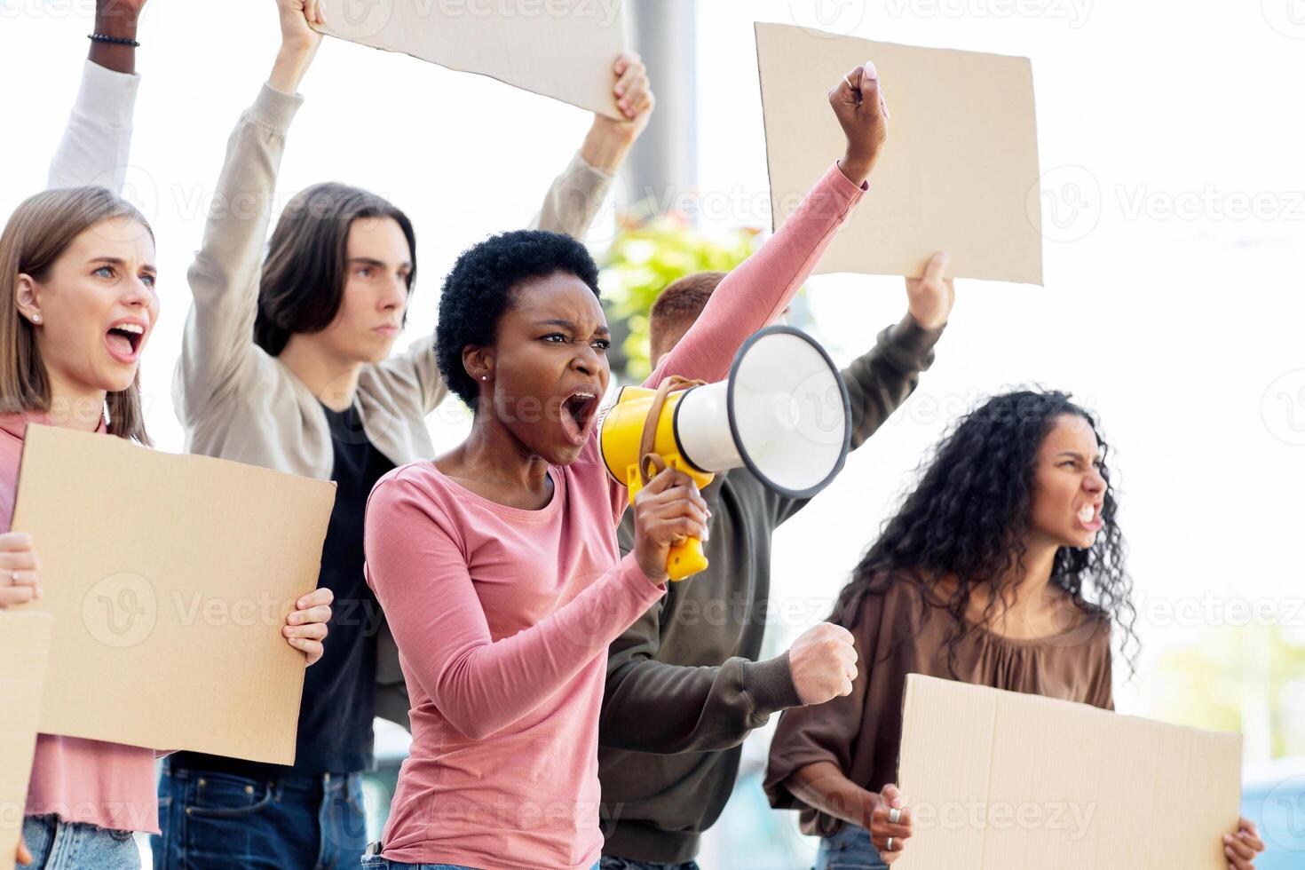 Multiethnic young demonstrators striking on the street, holding megaphone and empty placards. International group of people with blank banners protesting outdoors, defending human rights, side view photo
