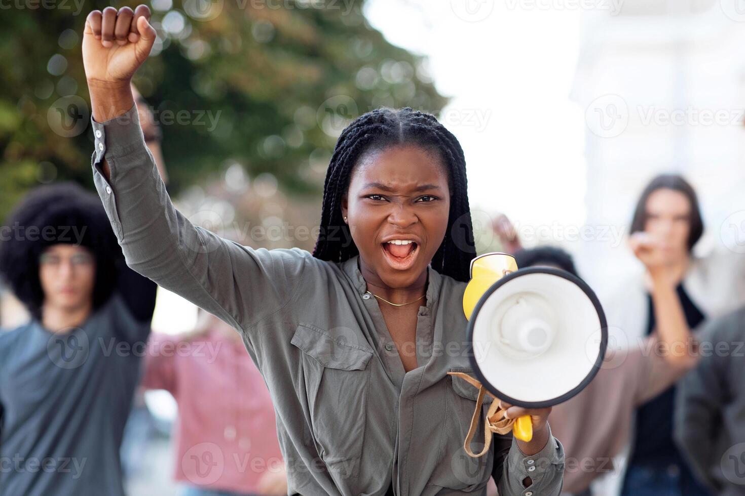 Emotional black lady activist with megaphone on the street, chanting slogans and raising fist up, young african american woman leading international group of activists, striking against lockdown rules photo