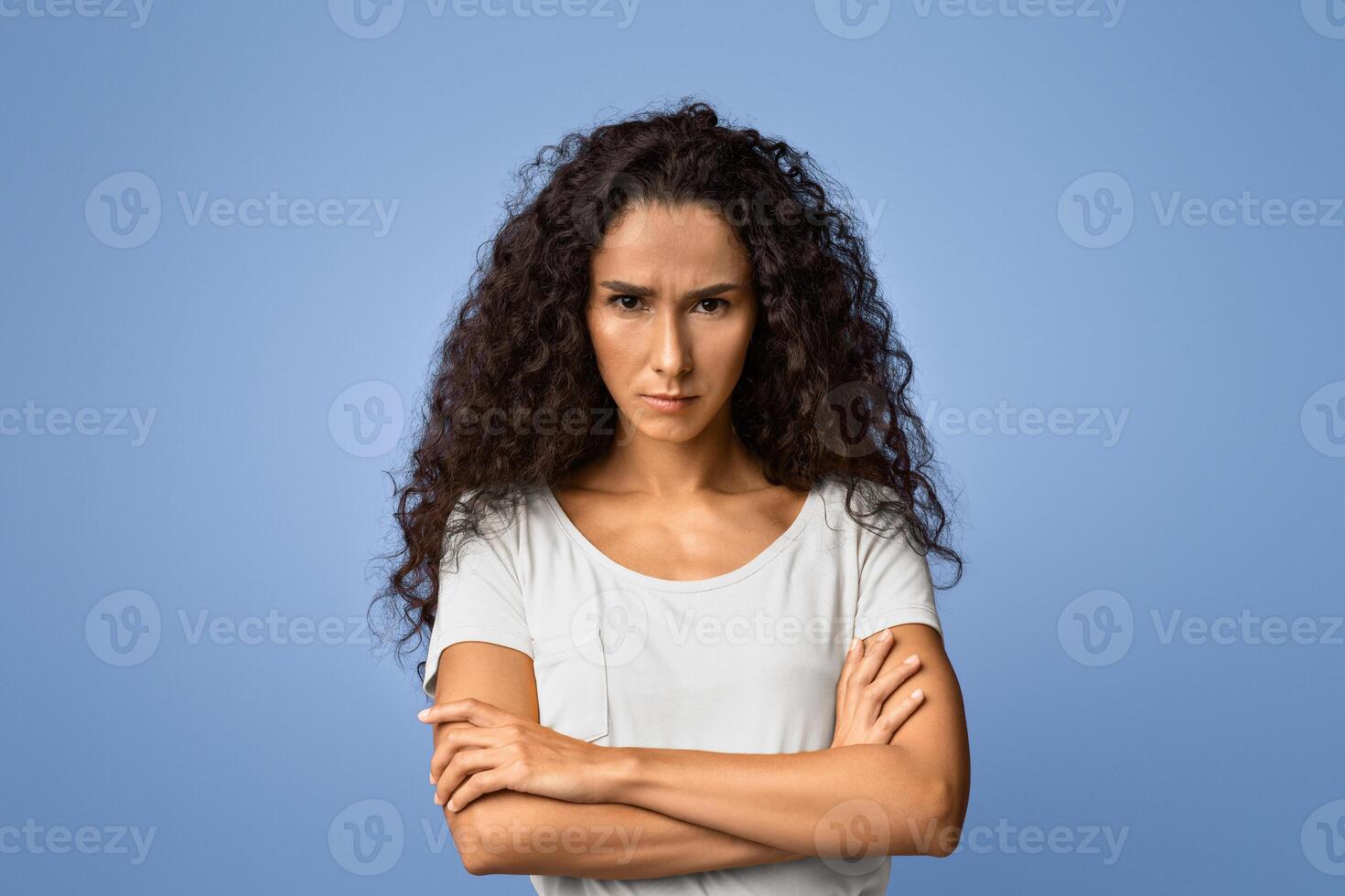 Grumpy Woman. Portrait of serious offended lady standing with crossed arms, posing over purple studio background, feeling angry and displeased, having bad mood, looking at camera, copy space photo