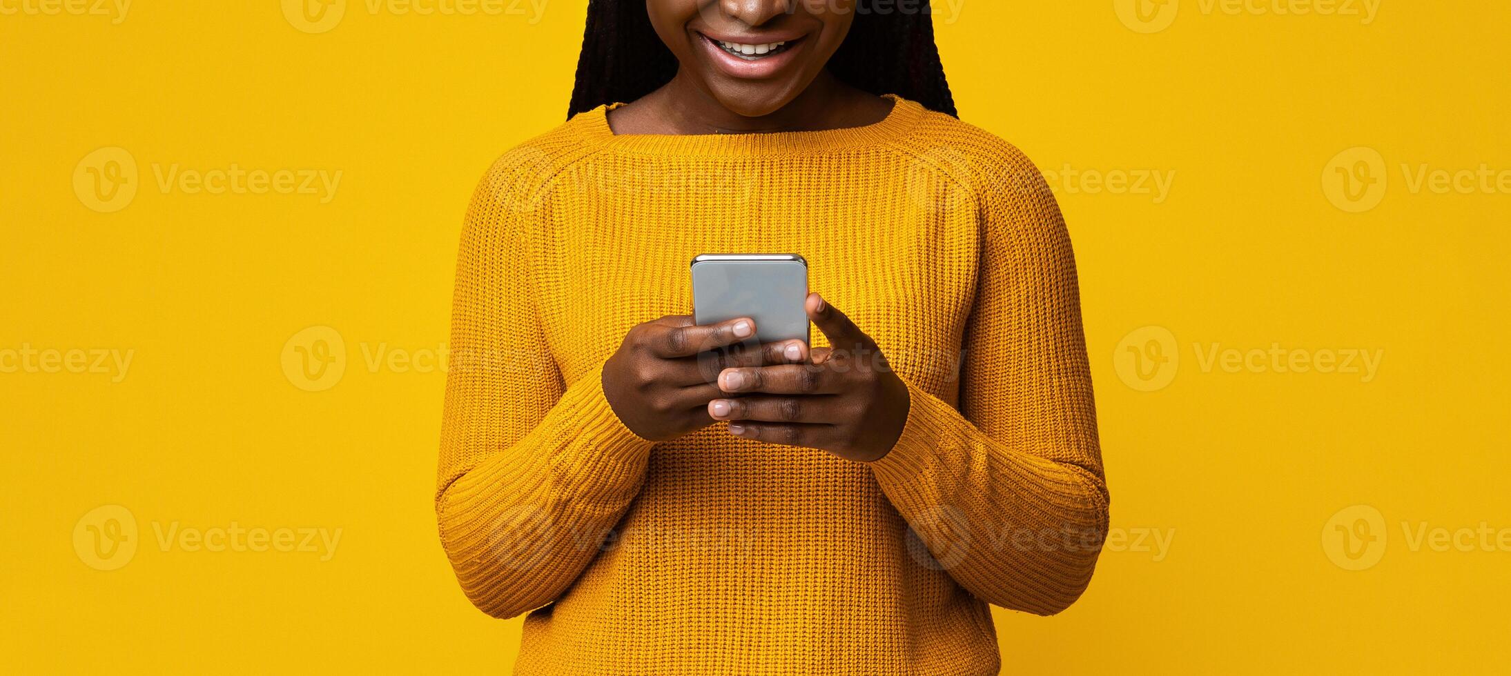 Smiling African American Lady Holding Smartphone, Texting With Friends On Yellow Background, Cheerful Black Female Using Cellphone, Enjoying Modern Technologies And Mobile Communication, Copy Space photo