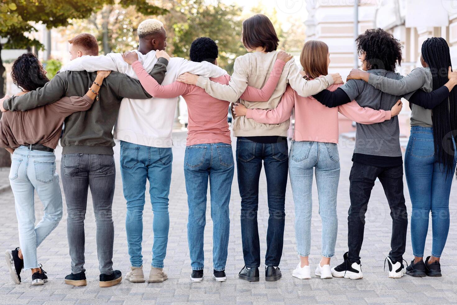 Back view of multiracial millennial demonstrators in casual standing in a row on the street, embracing, making live chain, fighting fot human rights, defying lockdown restrictions, panorama photo