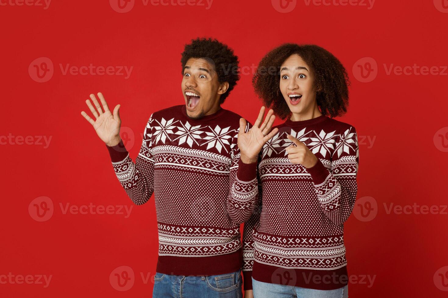 Shock and unexpected meeting. Amazed millennial african american male and female express positive emotions of surprise, gesturing and looking at empty space, isolated on red background, studio shot photo