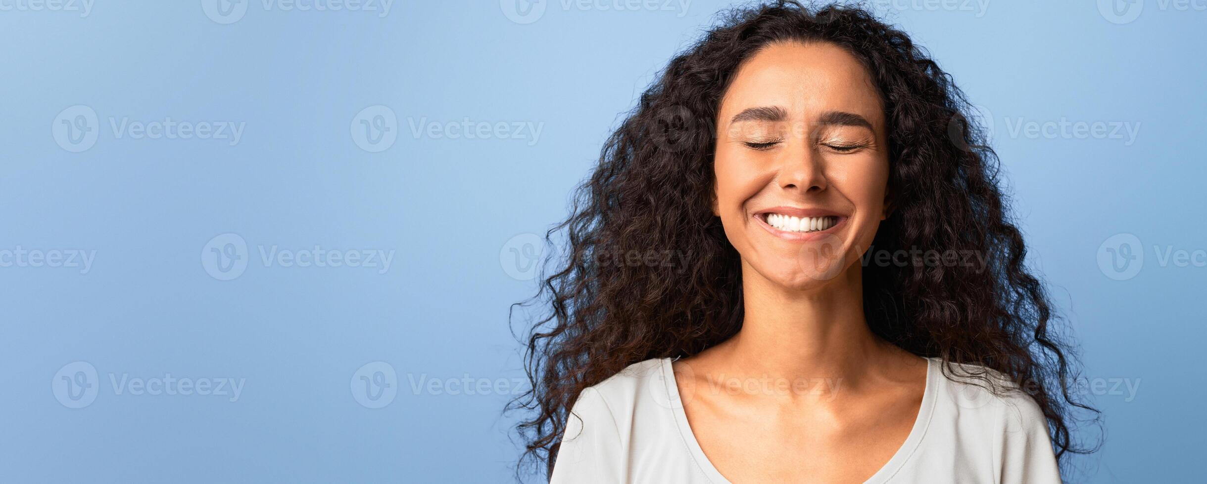Happiness. Happy Brunette Woman Smiling With Eyes Closed, Positive Young Lady With Curly Hair Sincerely Laughing While Posing Over Purple Background In Studio, Closeup Shot With Free Space photo