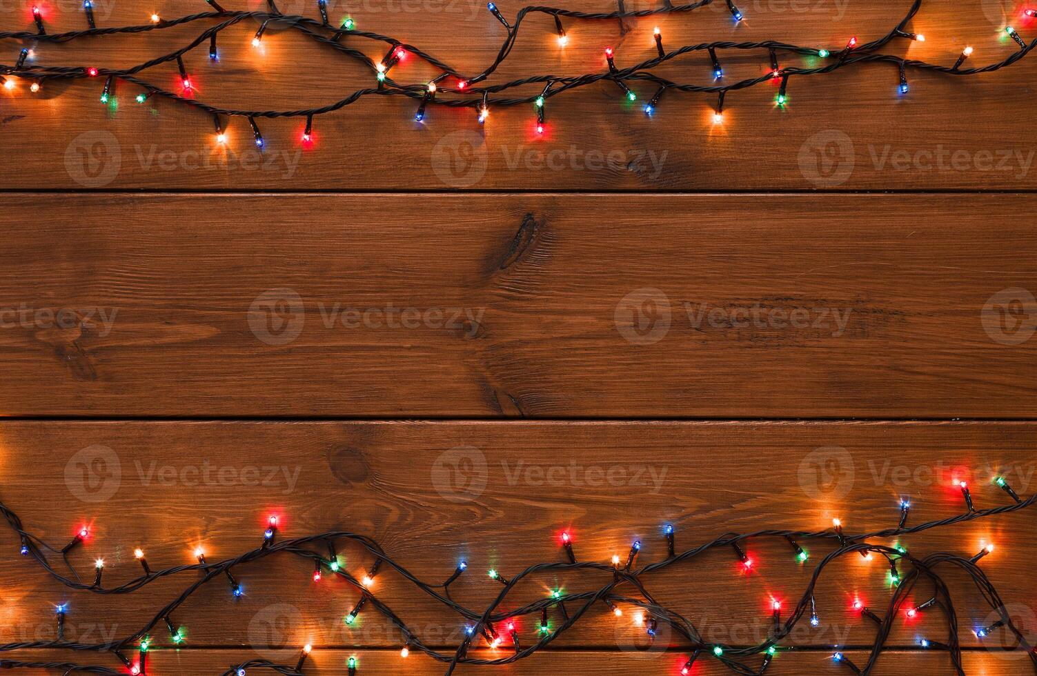 Christmas lights background, copy space. Holiday shiny colorful garland border top view on brown wooden planks surface. Xmas tree decorations, winter holidays illumination photo