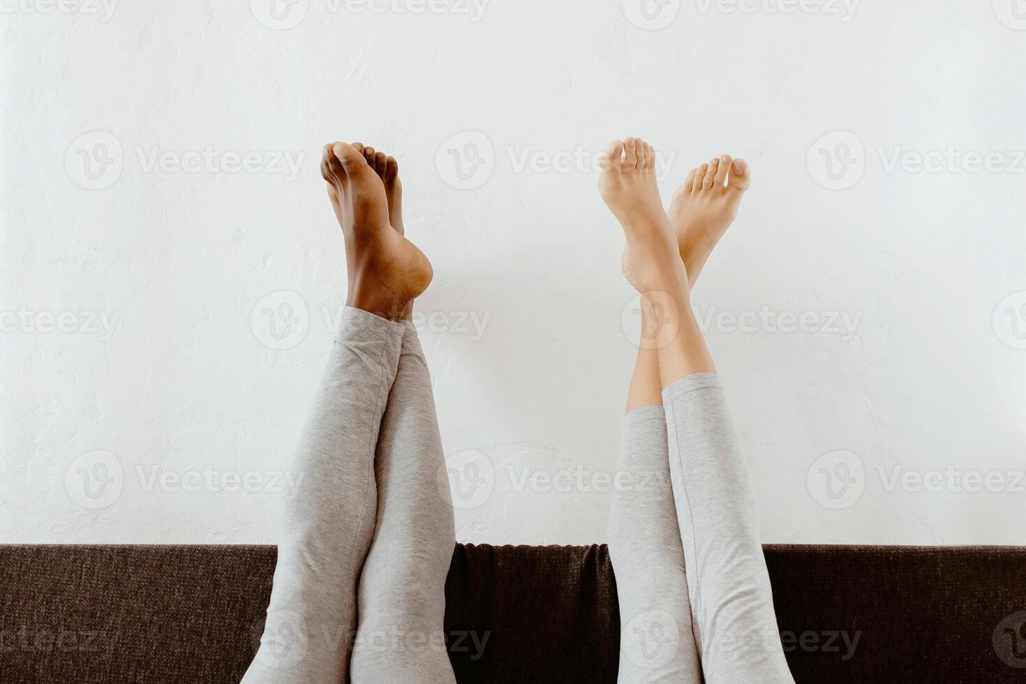 Free time in morning at home, relaxation, rest together, stay home at weekend. Millennial african american female and male with raised legs lie in bed in bedroom interior, empty space, vertical photo