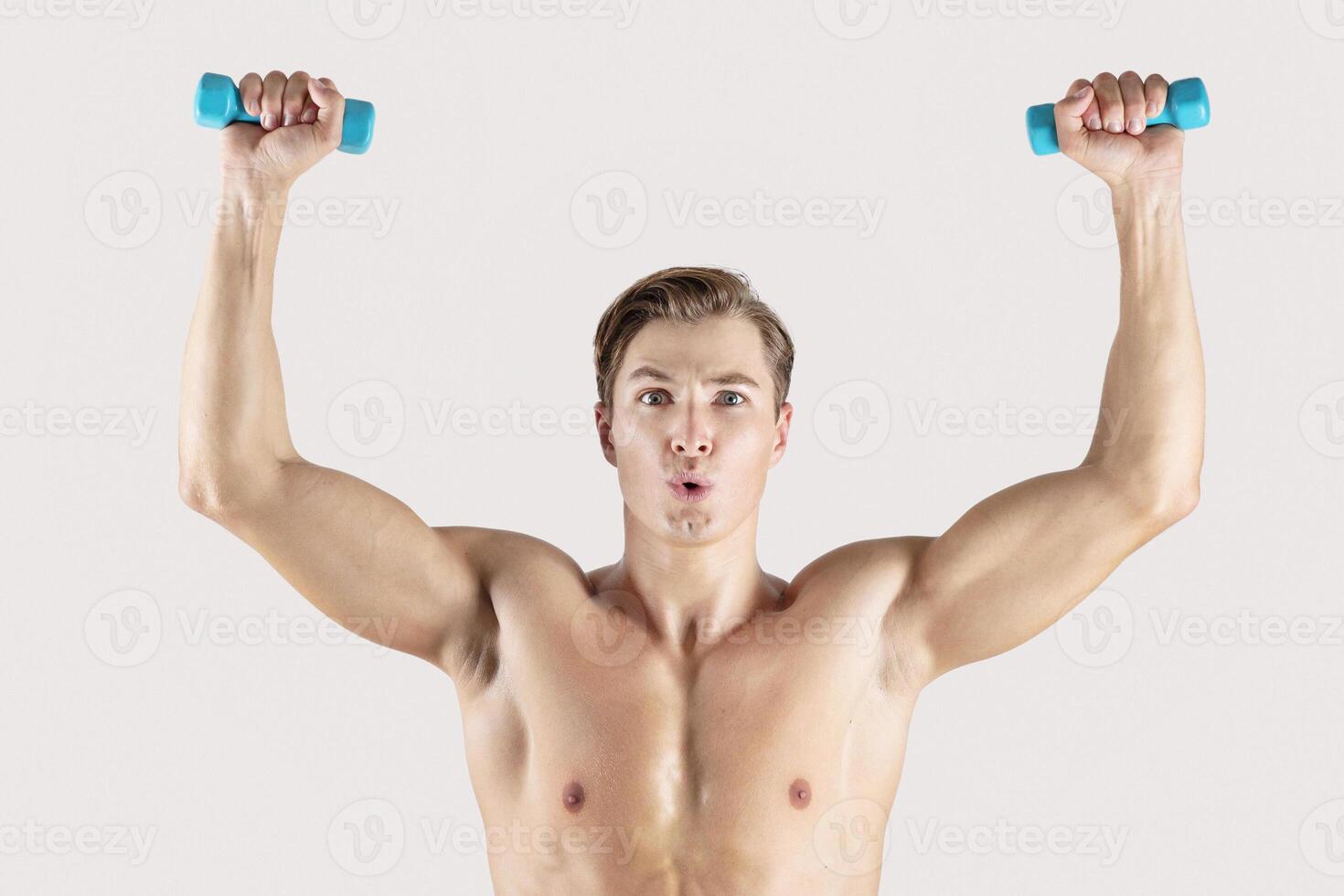 Strength workout. Handsome muscular man lifting small dumbbells on light studio background. Portrait of determined bodybuilder exercising with weights, leading healthy lifestyle photo