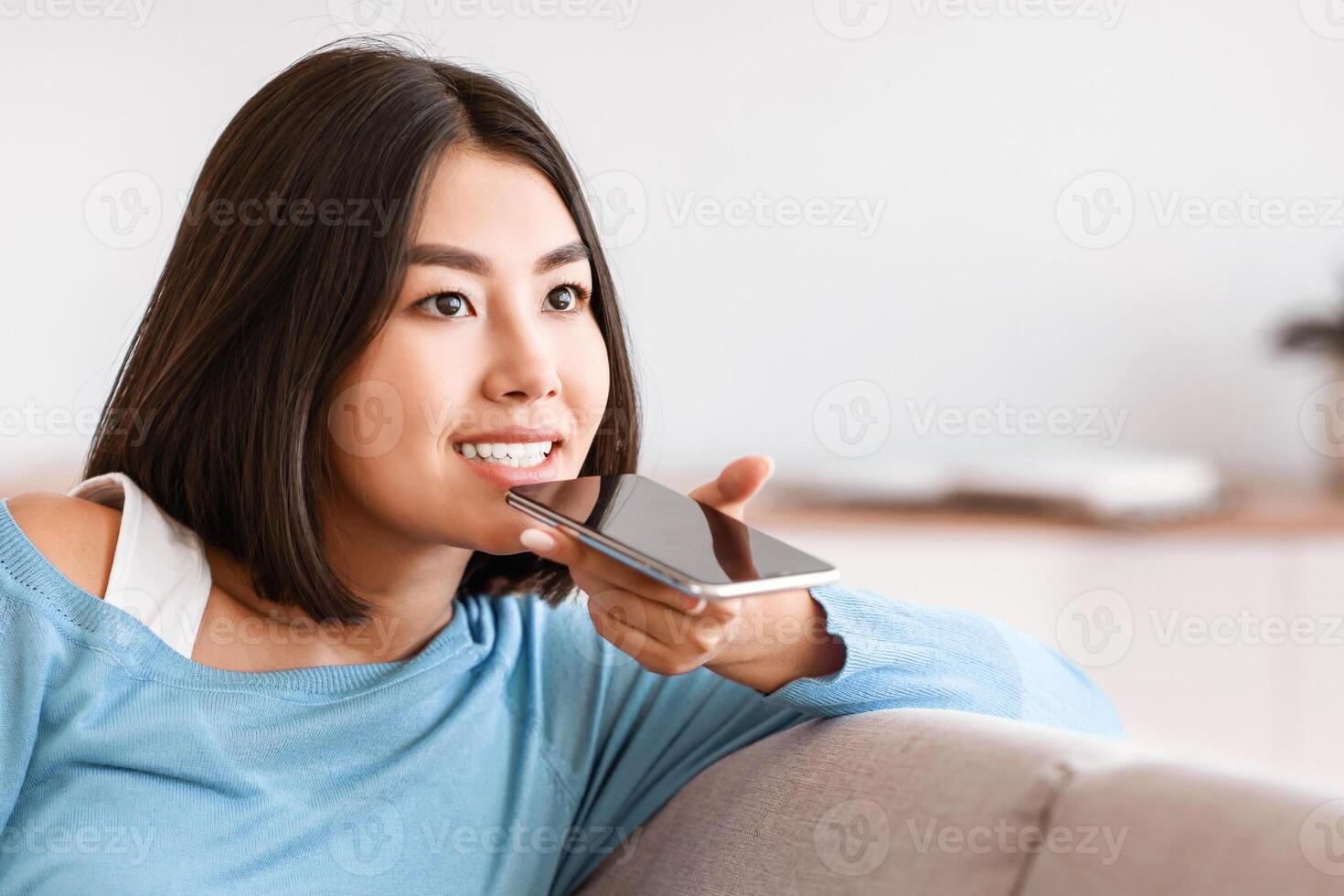 Voice Search. Closeup portrait of asian woman using smart phone voice recognition to send message, holding gadget near mouth. Lady speaking to virtual assistant, blurred background, copy space photo