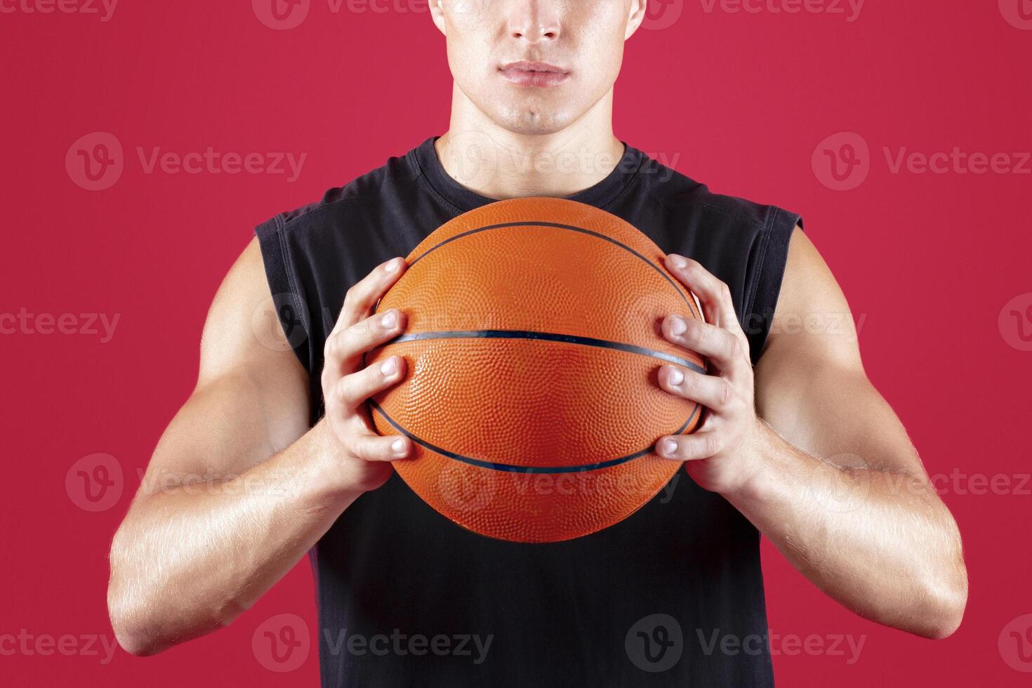 Portrait of determined young basketballer holding ball and looking at camera on red studio background. Active streetball player motivated to win match, taking part in tournament photo