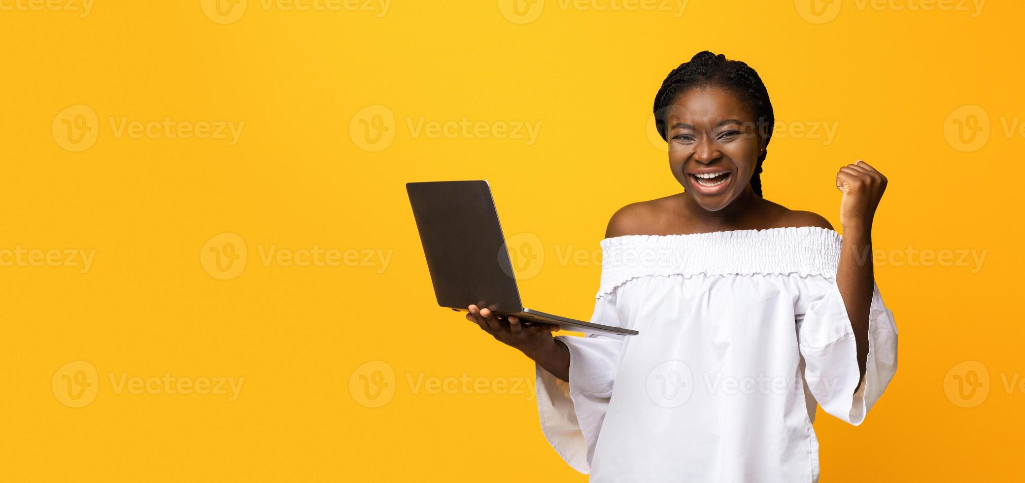 Yes. Excited African American Lady Celebrating Success With Laptop, Shaking Fist, Cheerful Black Woman Holding Computer, Won Online Lottery, Got Visa Approval, Standing Over Yellow Studio Background photo