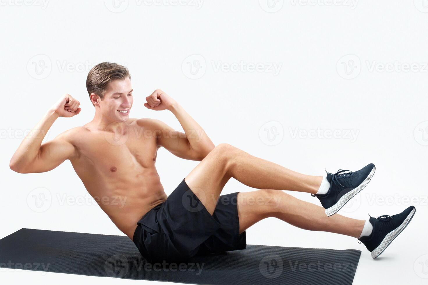 Strong young guy exercising on sports mat, working on abs muscles over light studio background, copy space. Handsome millennial sportsman with naked torso doing core workout. Active lifestyle concept photo