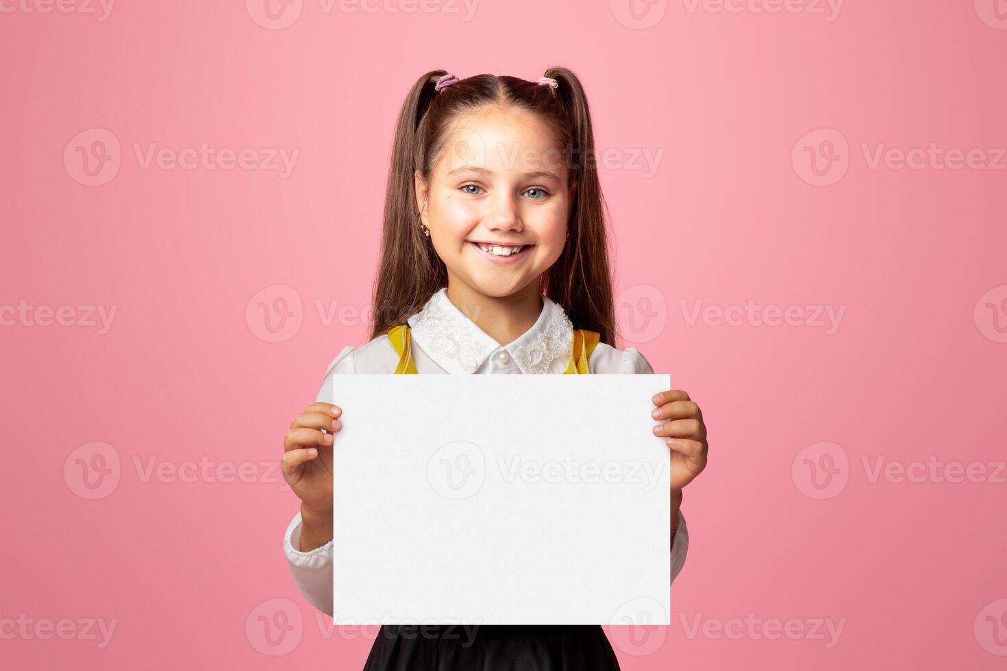 Primary education. Small schoolgirl with happy smile holding sign with free space, isolated on pink background, studio shoot photo