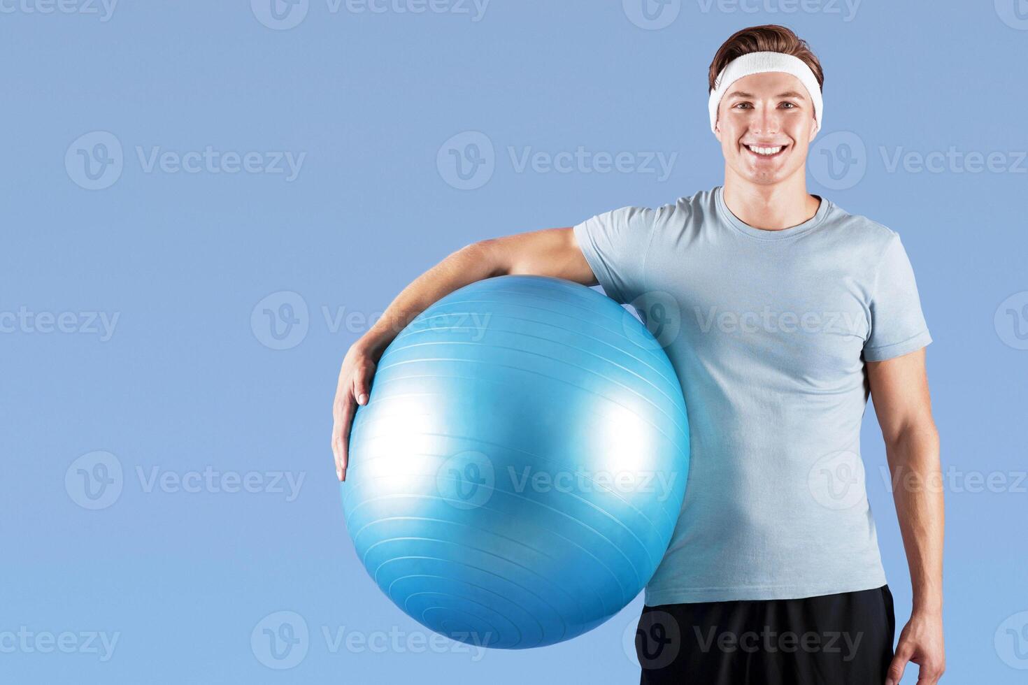 Cheerful millennial athlete with fitness ball smiling and looking at camera on lilac studio background. Portrait of happy young sportsman ready for aerobic workout. Healthy living concept photo