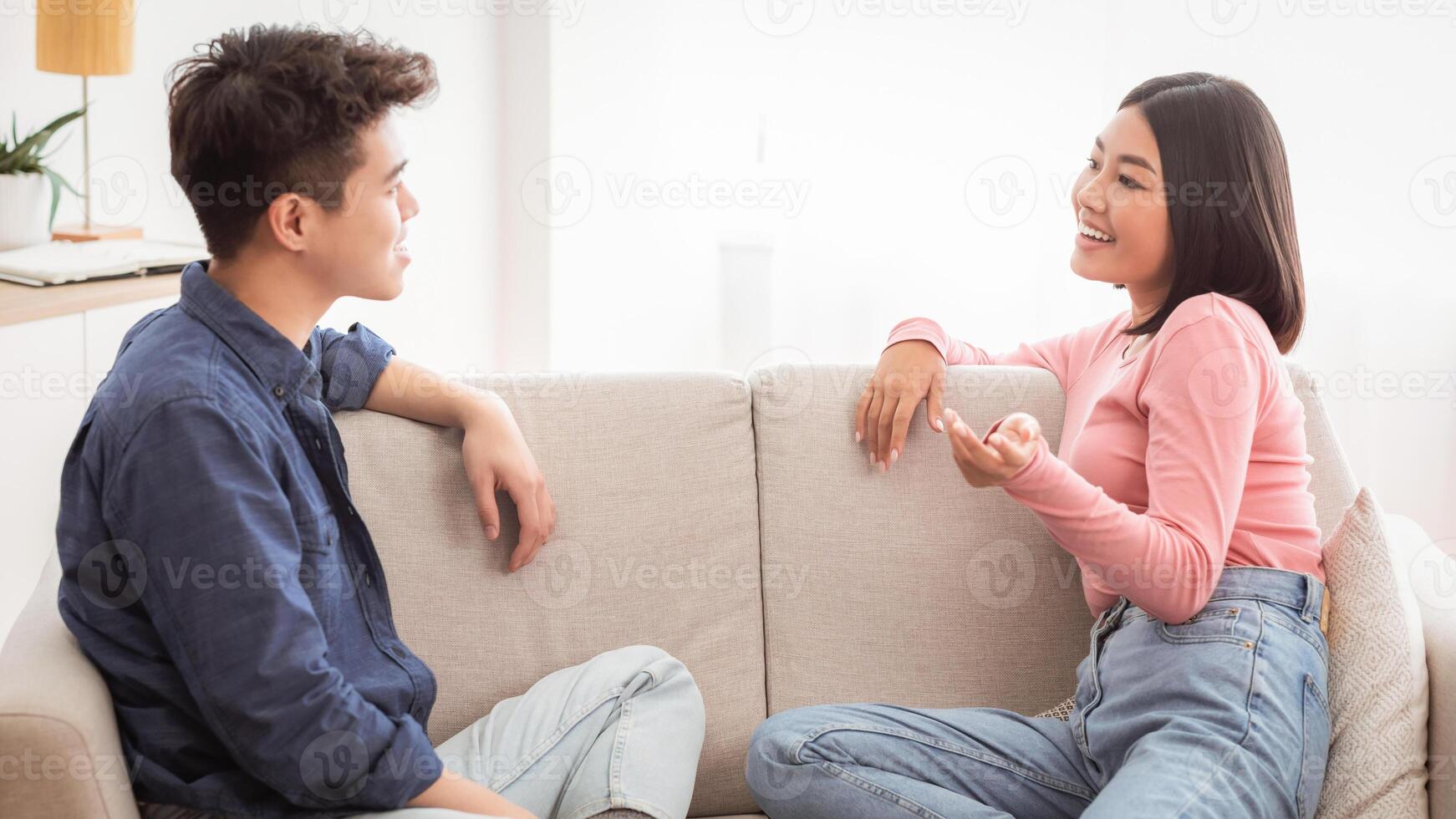 Dating Asian Couple Talking And Flirting Enjoying Conversation Sitting On Couch In Living Room At Home On Weekend. Romantic Relationship And Flirt Communication, Stay-At-Home Date Concept photo