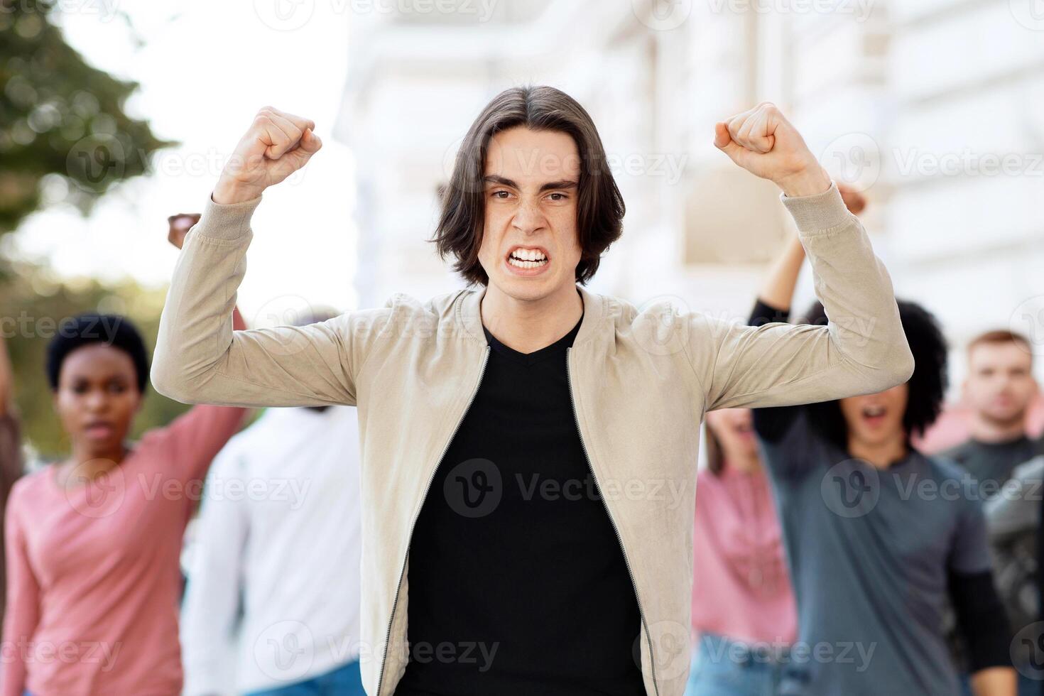 Young man leading multiracial group of people protesting against lockdown on the street, showing government attitude. Demonstrators making riot on the street, chanting slogans, need for money photo