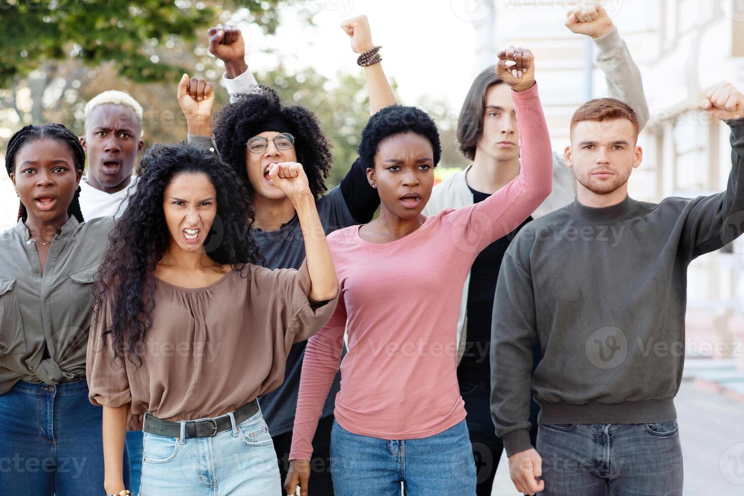 Climate change protest concept. International group of young people making strike on the street, chanting slogans and raising fists up, demanding from government saving planet, reducing pollution photo
