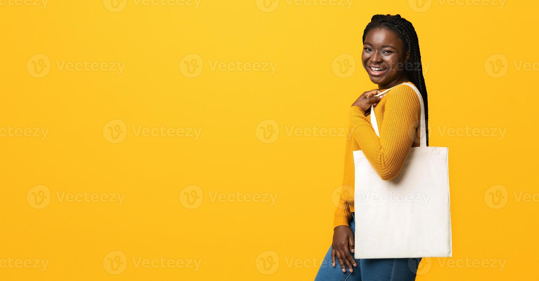 Smiling African American Woman With Blank Textile Tote Eco Canvas Shopping Bag Posing Over Yellow Studio Background, Smiling At Camera, Empty Copy Space For Your Logo, Advertisement Or Branding photo