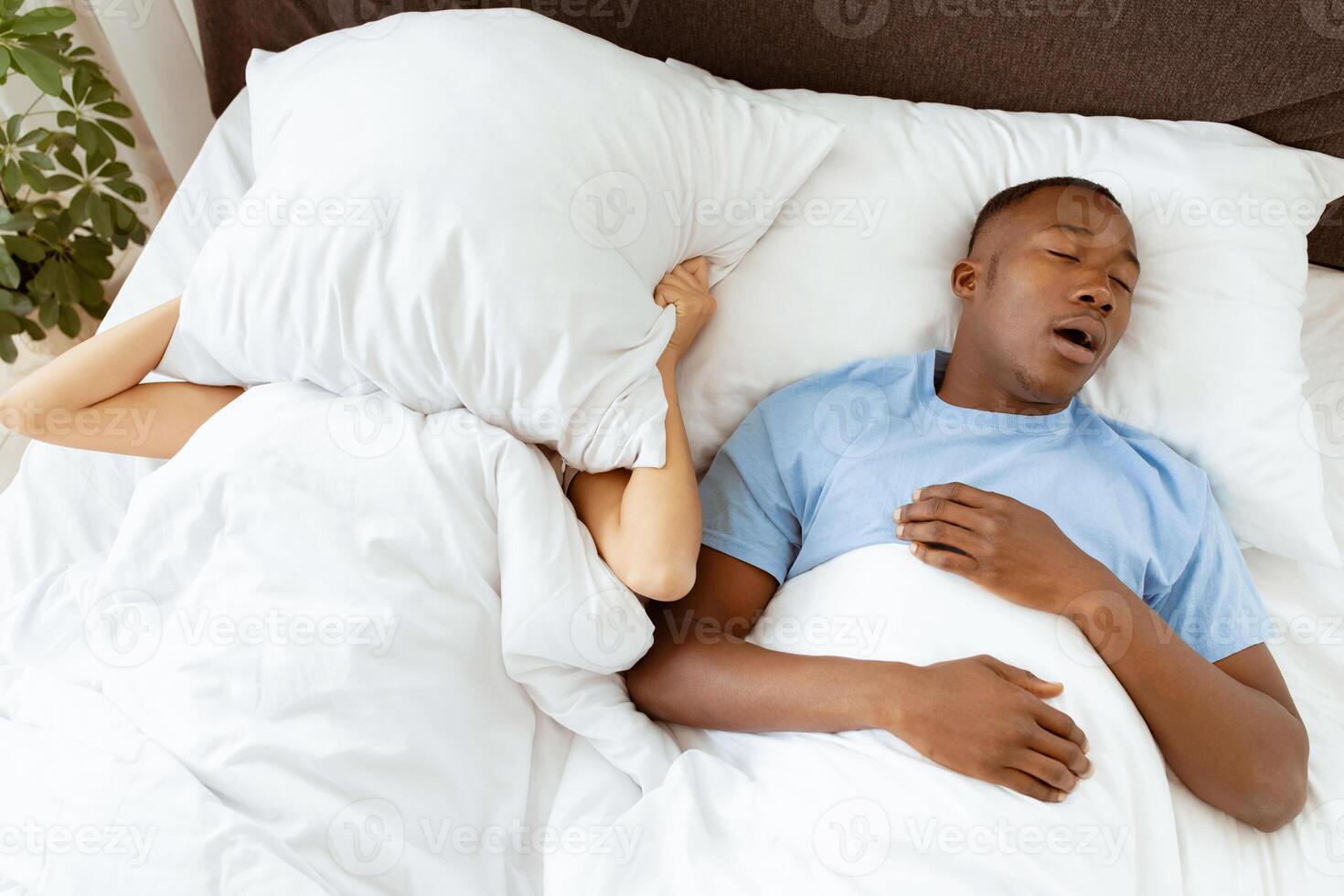 Cannot sleep, problems, apnea, chronic depression, divorce with spouse. Sad young african american lady covers face with pillow so as not to hear noise from husband in bedroom, copy space, top view photo