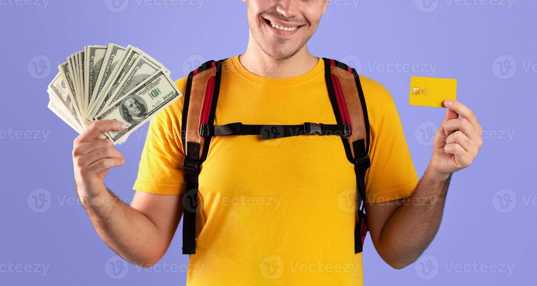 Planning travel budget concept. Portrait of funky young man with backpack, credit card and money smiling and looking at camera over blue studio background photo