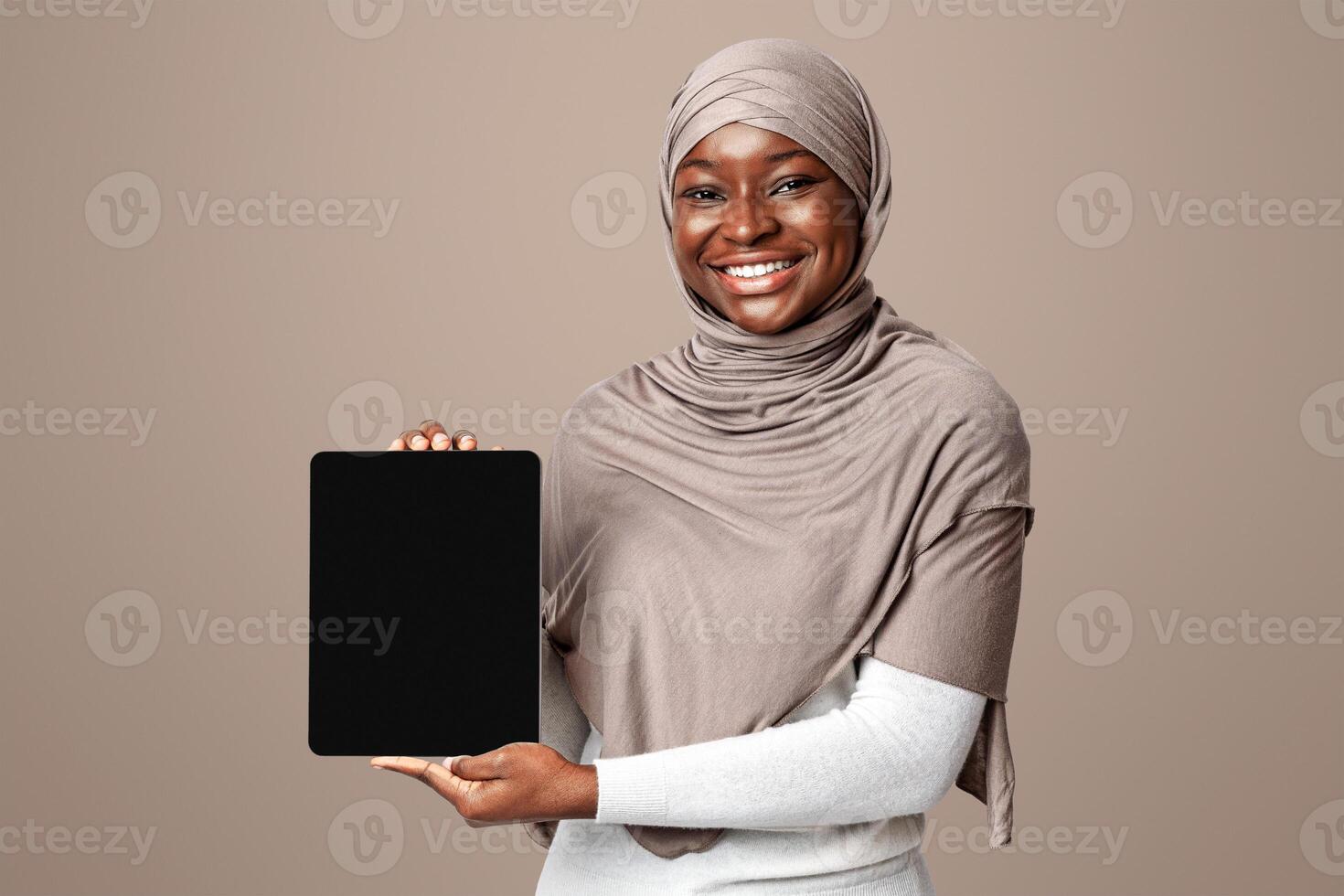 Mockup Image Of Black Muslim Lady In Hijab Holding Digital Tablet With Blank Screen, Demonstrating Free Copy Space For Your App Or Website Design, Smiling Woman Standing Over Light Studio Background photo