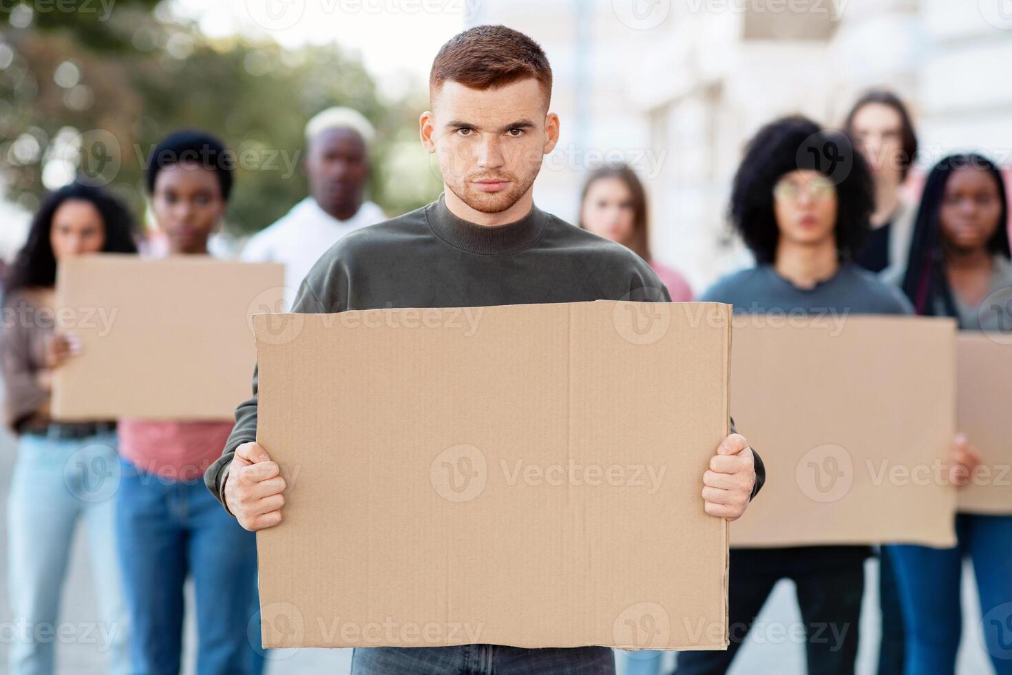 Confident guy leading international group of demonstrators on the street. Young man activist over multiracial group of people with empty placards protesting for human or animal rights photo