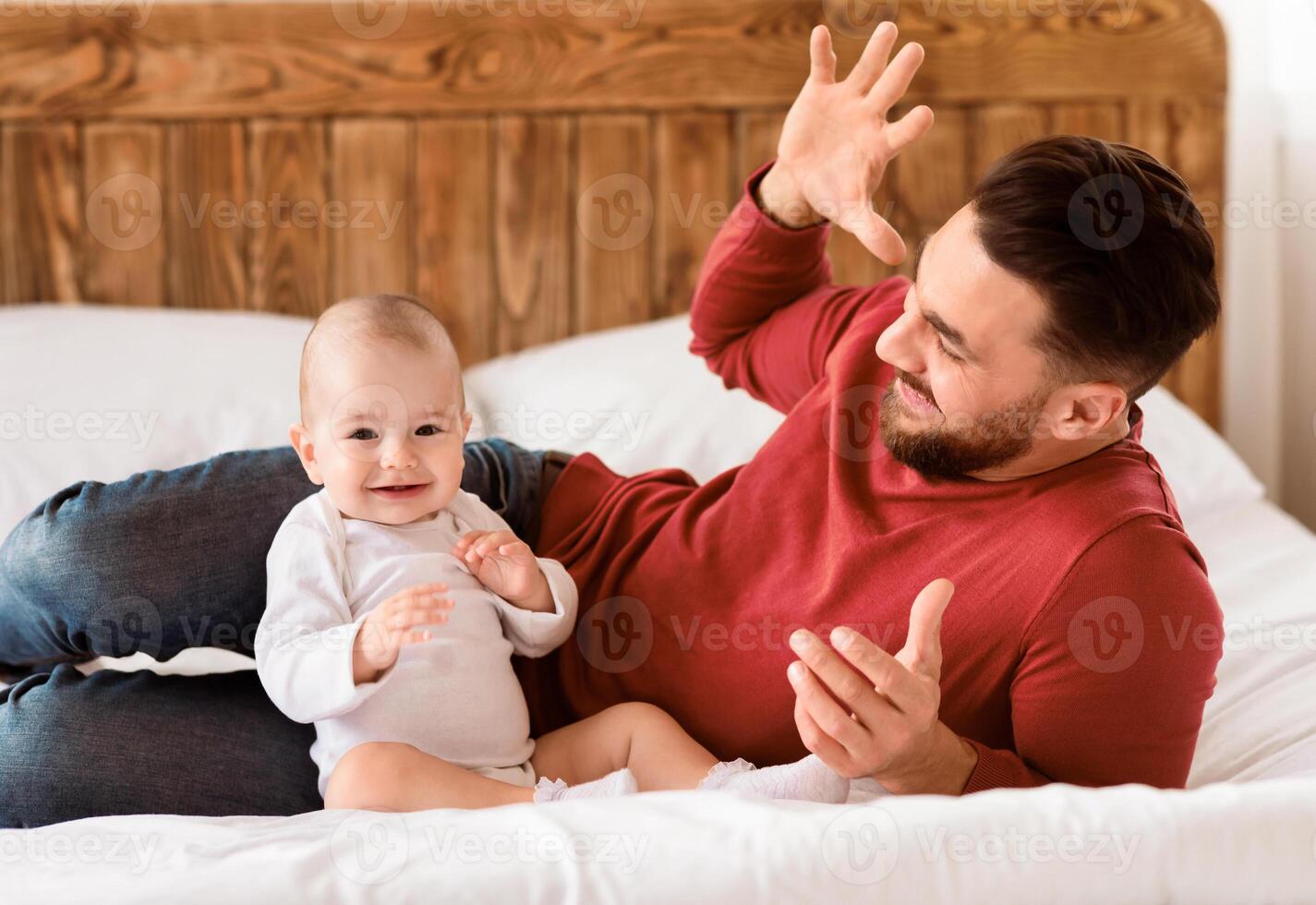 Young Father Cuddling And Bonding With Little Baby Toddler Lying On Bed At Home. Loving Daddy And His Newborn Daughter Spending Time Together Laughing And Playing. Fatherhood, Joy Of Parenting photo