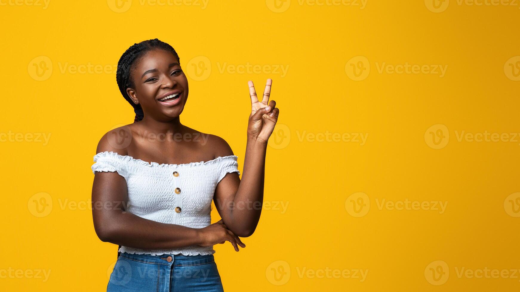 Cheerful Black Woman Showing Peace Gesture While Posing Over Yellow Studio Background, Positive African American Lady In Stylish Clothes Gesturing V-Sign, Having Fun And Smiling At Camera, Copy Space photo
